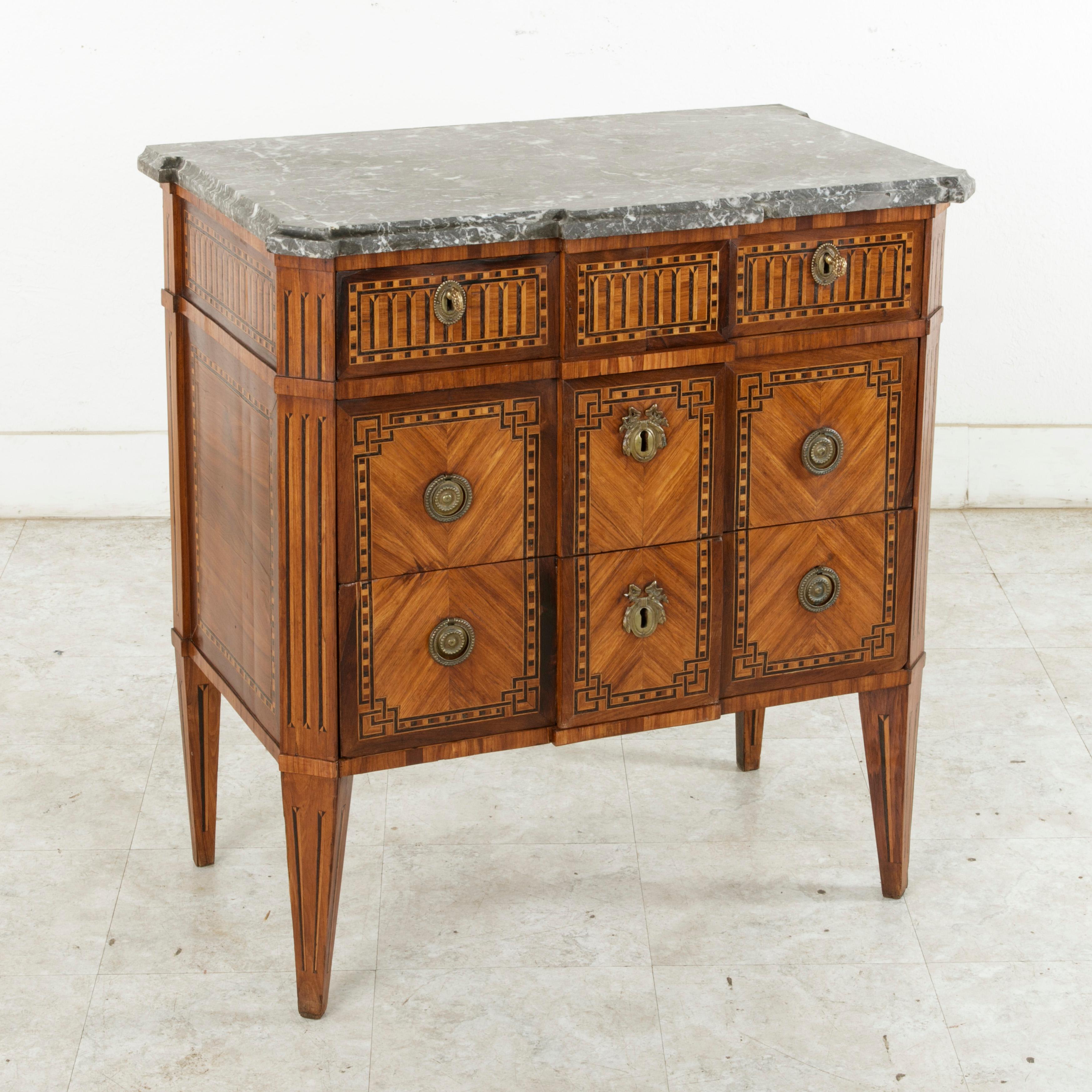 Found in eastern France, this rare smaller scale late 18th century, French Louis XVI period chest features a beveled Saint Anne marble top and a geometric marquetry facade of rosewood, lemon wood, and ebonized pear wood. A marquetry gallery forms