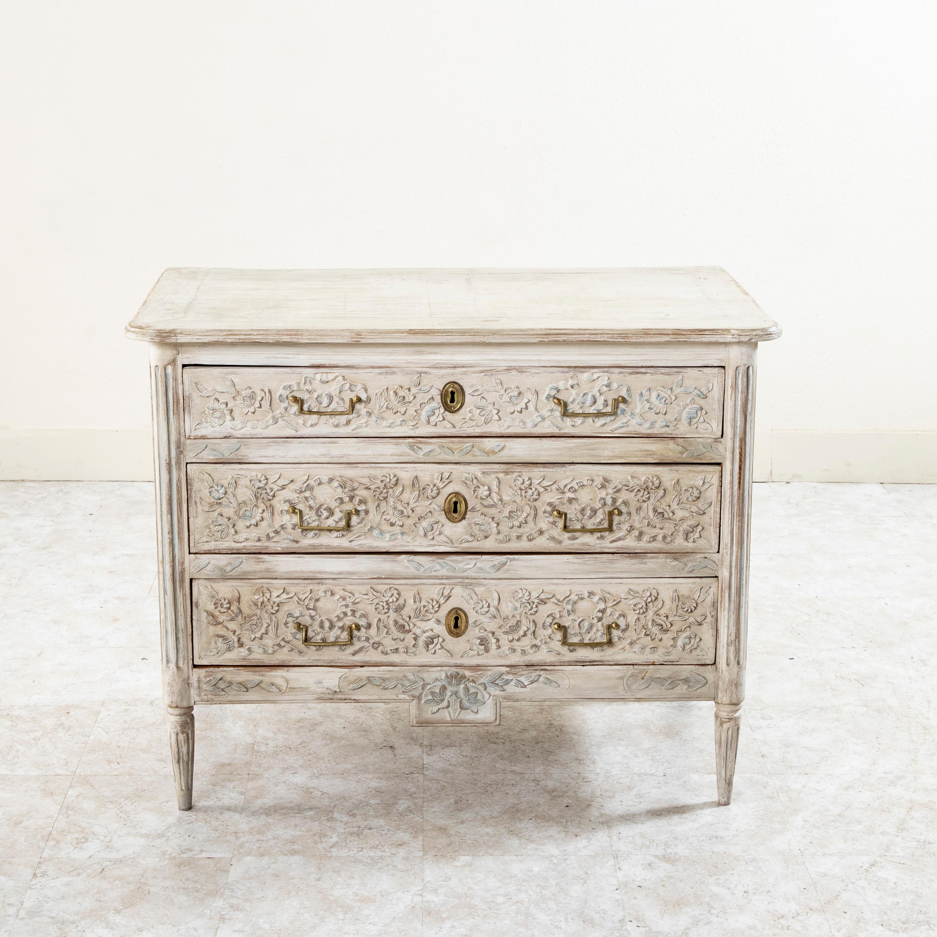 From the region of Provence in southern France, this late eighteenth century Louis XVI period painted commode or chest of drawers features hand pegged paneled sides and hand carved details of classic knotted ribbons and garlands of flowers on the