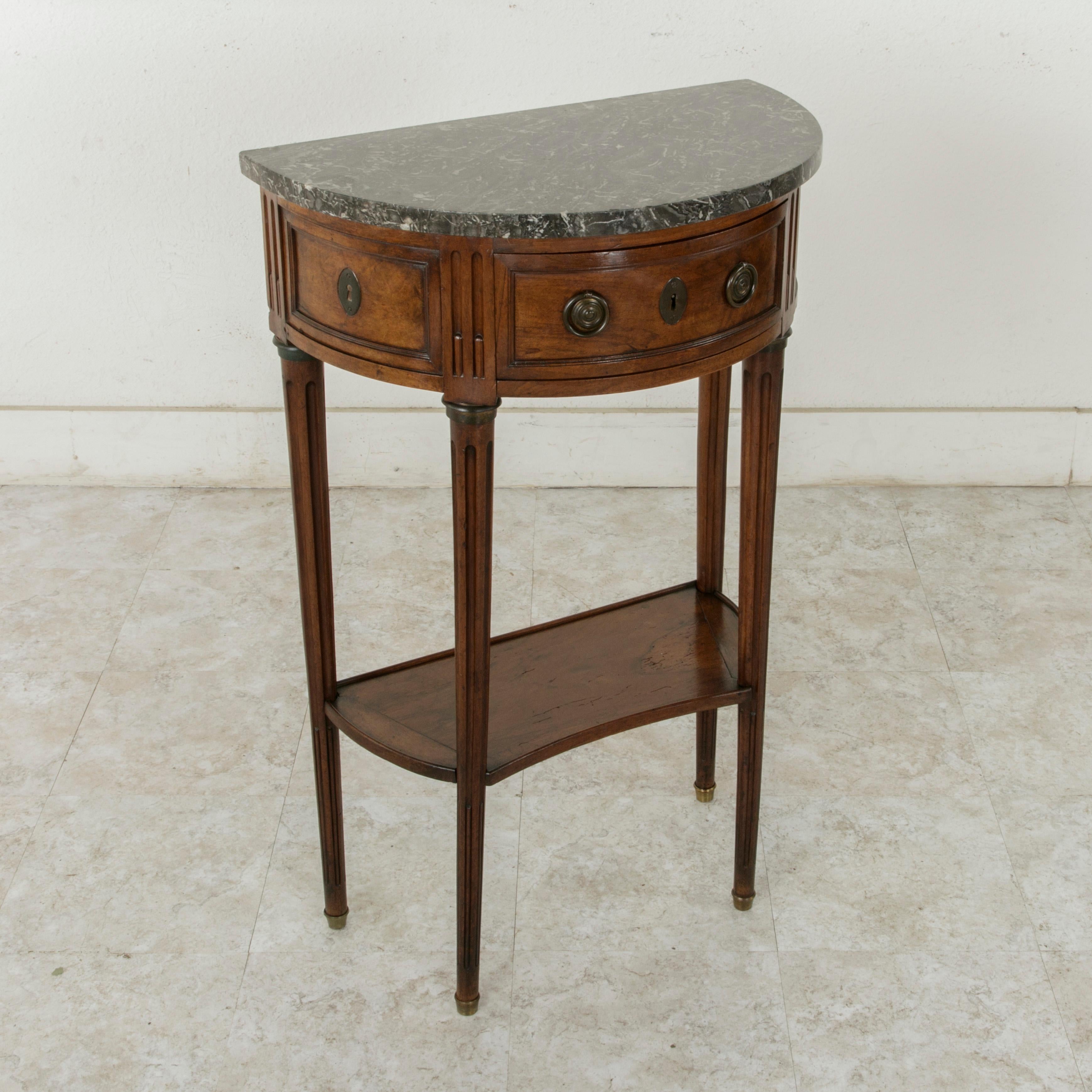 This Late 18th century Louis XVI period walnut demilune console table is from the city of Dijon in the region of Burgundy, France. Attributed to cabinet maker Jean Demoulin (1715-1798), this piece features fluted corners and cable fluted tapered