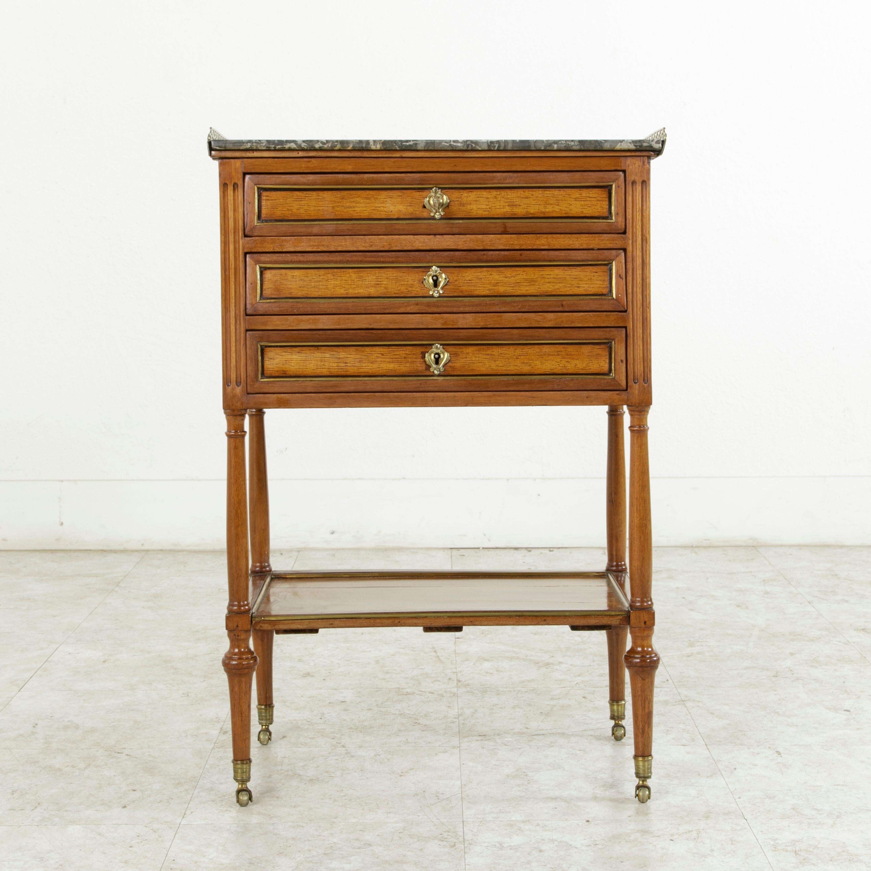 This unique late 18th century French Louis XVI period walnut side table or nightstand features fluted corners and inset bronze banding around its rosewood facades. A pieced bronze gallery surrounds its Saint Anne marble top on three sides. Its three