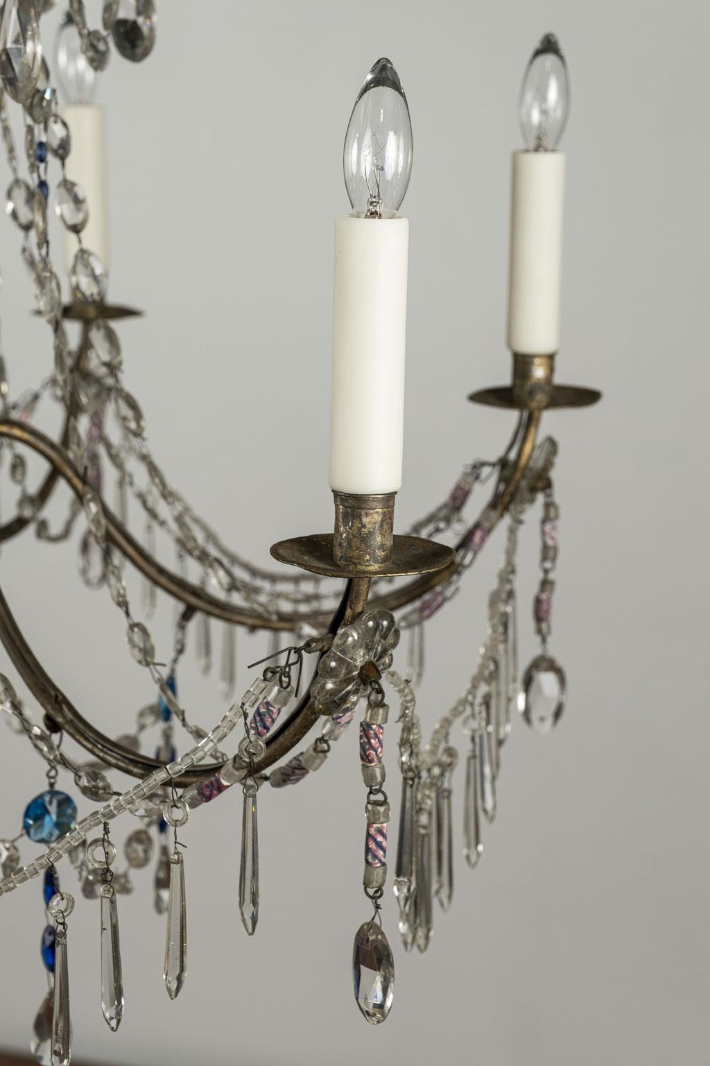 Late 18th century Genoese chandelier consisting of a carved giltwood body, original eight iron arms and original and later crystal prisms (clear and colored). Hand-blown and pressed glass decoration and beading. This Genoa chandelier includes extra