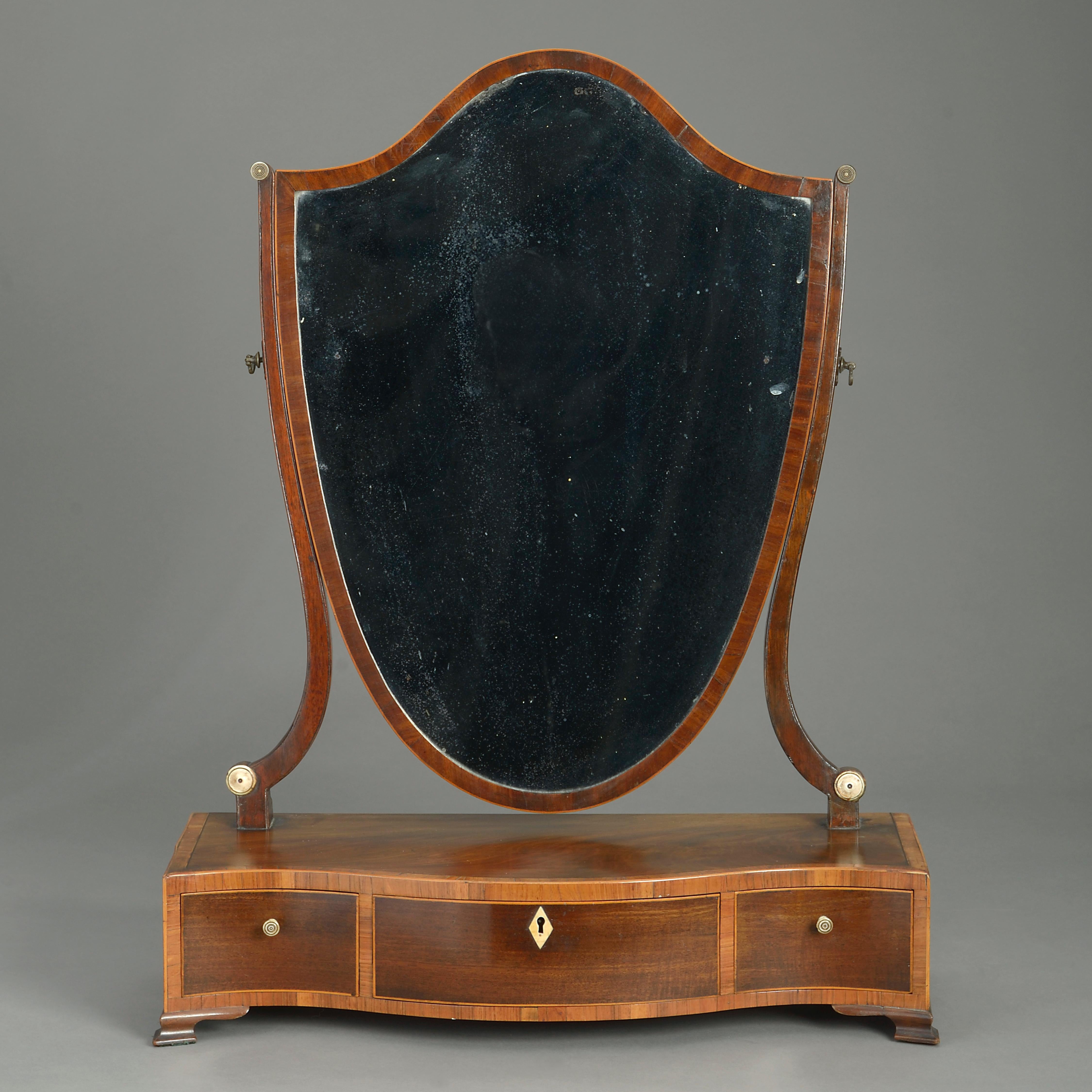 A very fine late 18th century George III period mahogany toilet mirror, the back of shield form, held by two upright supports and set upon a serpentine base of three drawers, each with tulipwood crossbanding, all terminating in bracket feet.