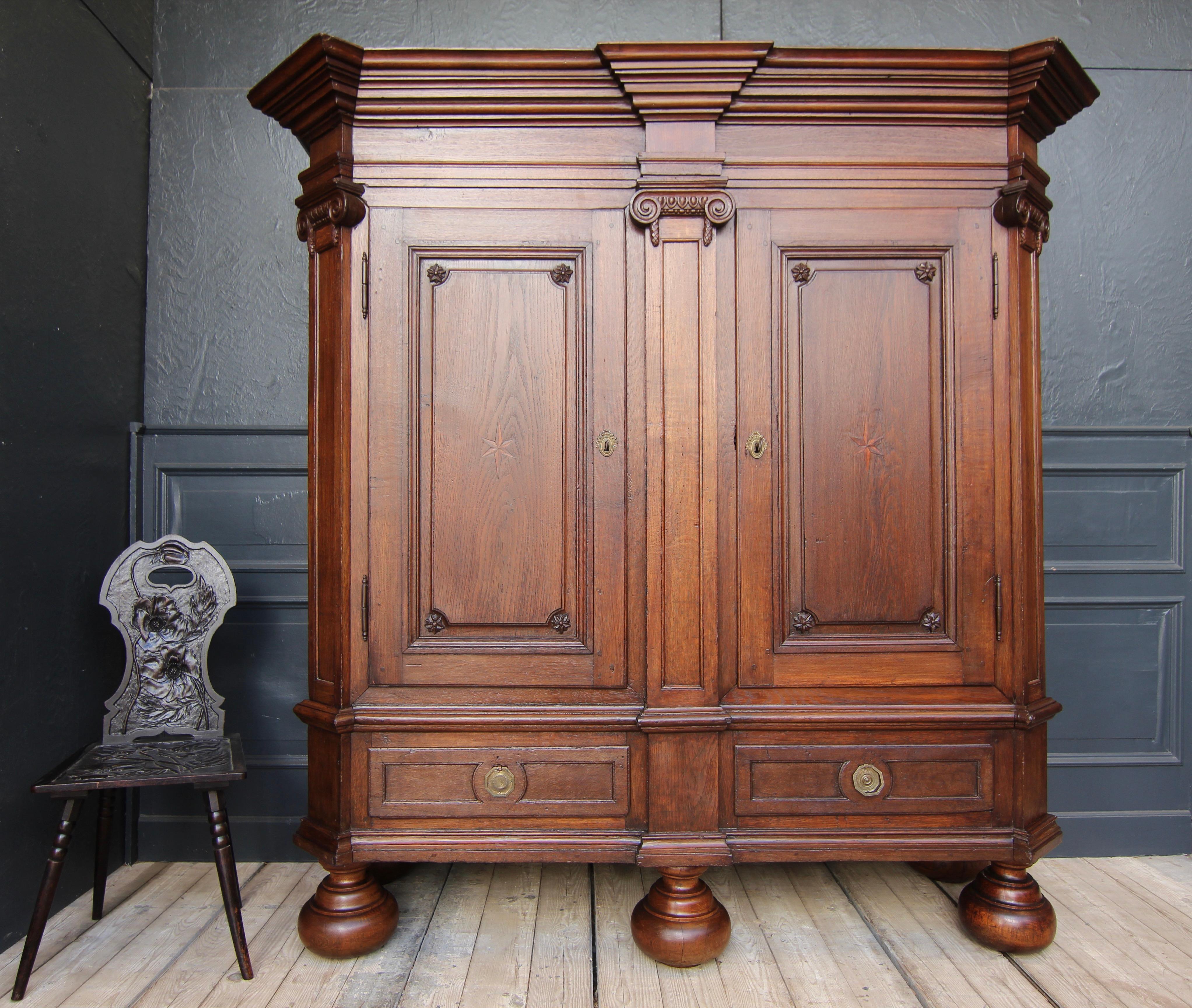 A late 18th century German neoclassicism Louis XVI armoire or cabinet. 

Two-door dismountable oak corpus with corner slopes standing on 5 ball feet. Subdivided by 3 pilasters with Ionic capitals. Overhanging cranked cornice with several profiles.