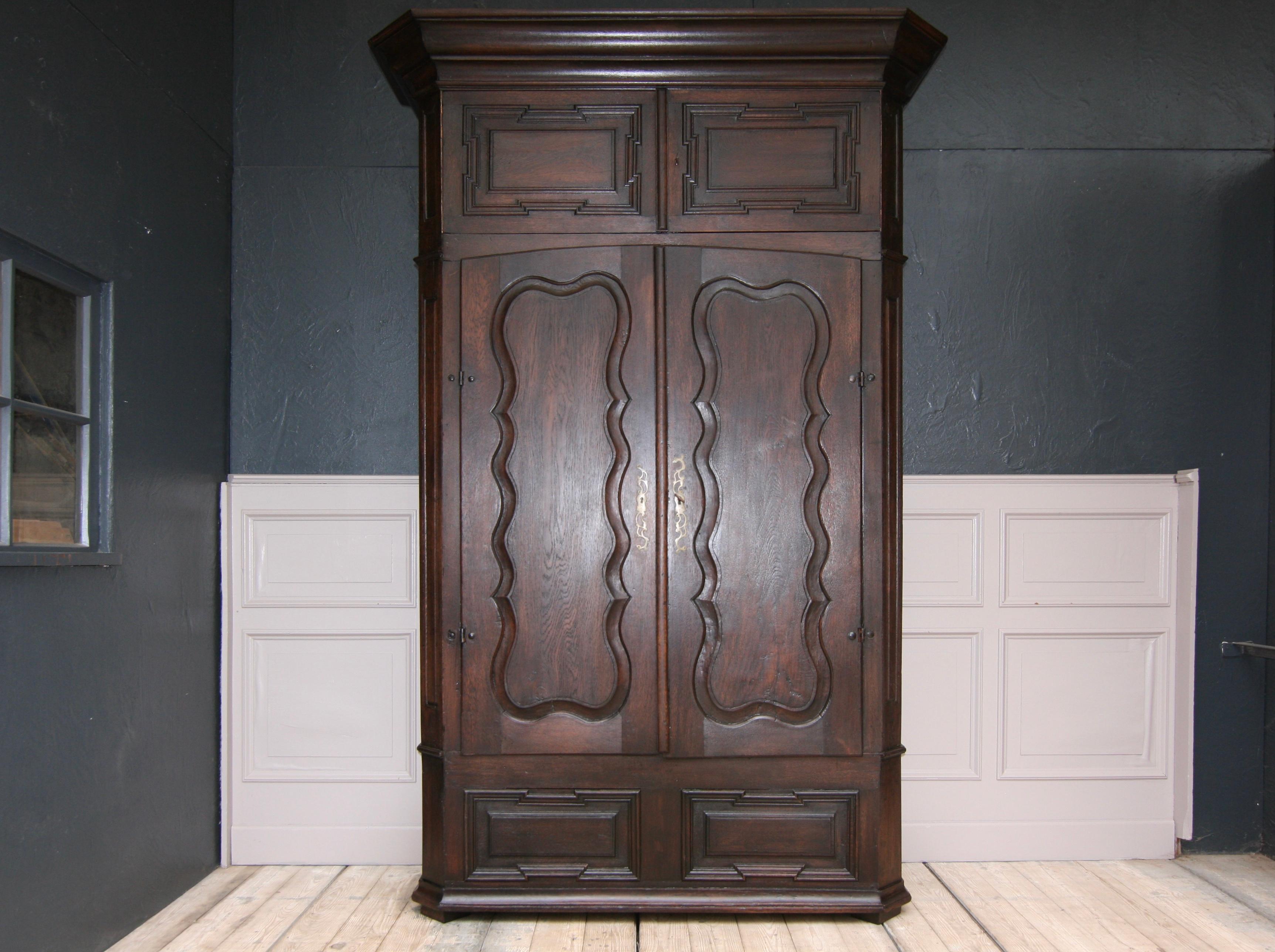 Antique cabinet or cupboard from a German monastery. Made of solid oak. Mostly from the late 18th century.

Body with beveled corners and protruding header. Cassettes on the side. Two large doors with curved, profiled panels. Above that, there are