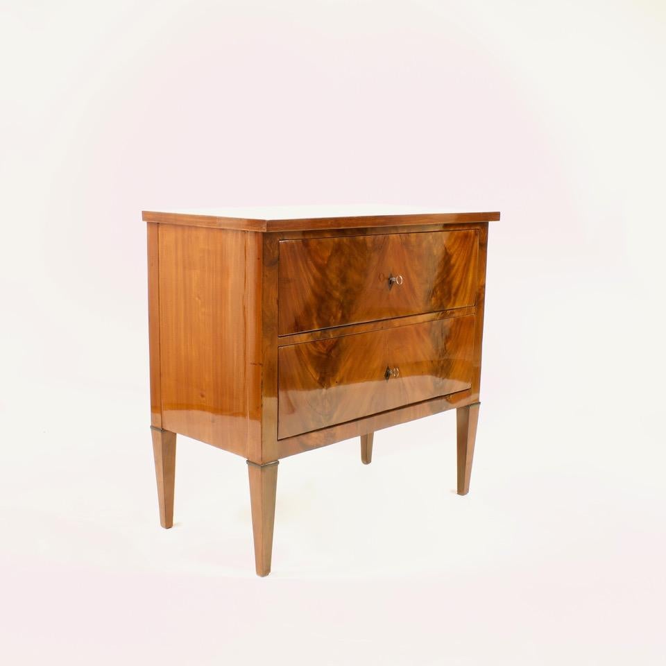 Late 18th century German neoclassical chest of drawers or commode

Straight rectangular body standing on four downward tapering legs with two drawers extending across the entire front. Finishing wooden top plate with fine mirror veneer.
