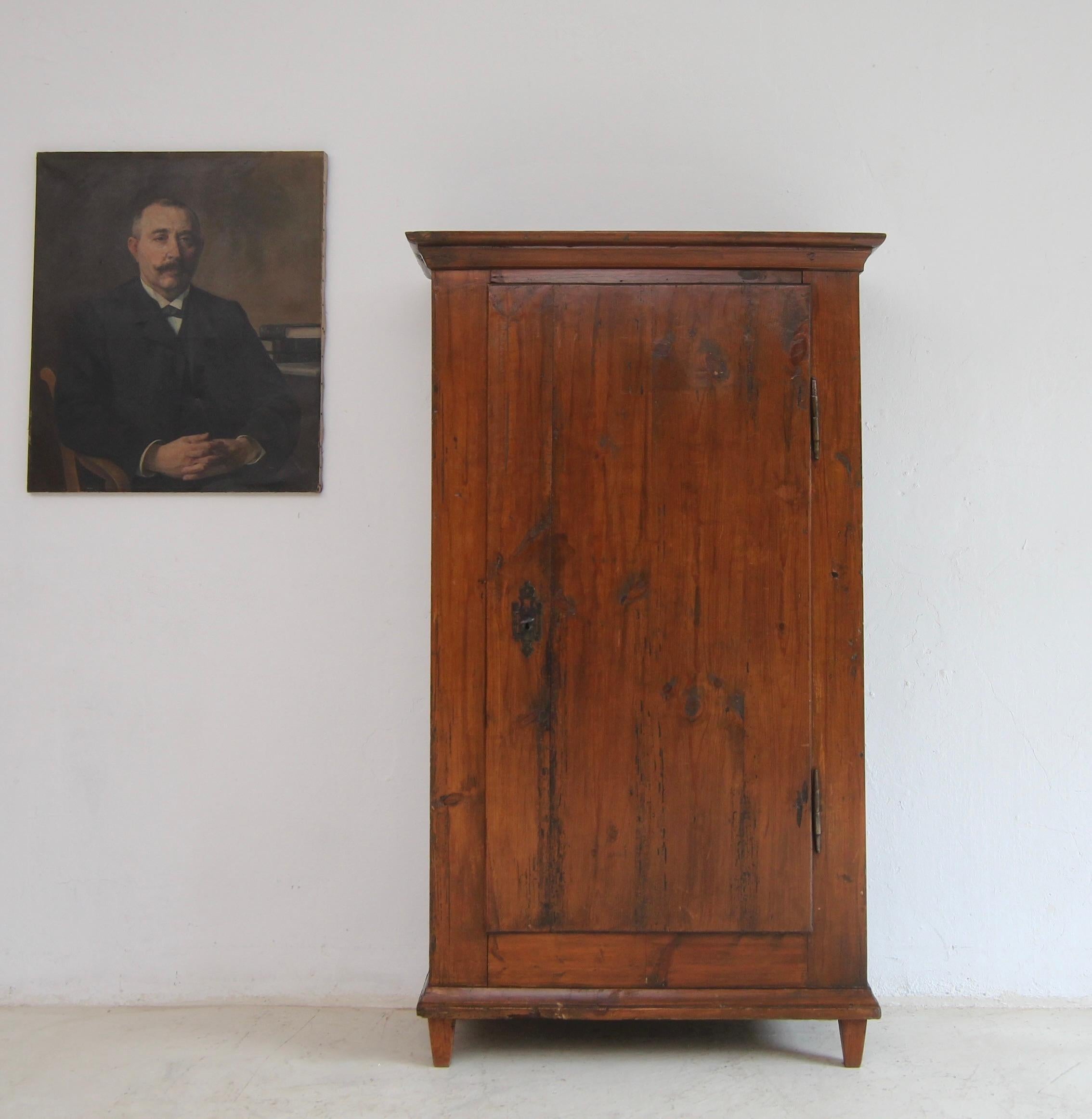 A provincial classicist 1-door cabinet made of pine. Probably South German, around 1800. Ready for everyday use.

Straight-lined stained pinewood body standing on 4 tapered square pointed feet with one door on hand-forged external iron