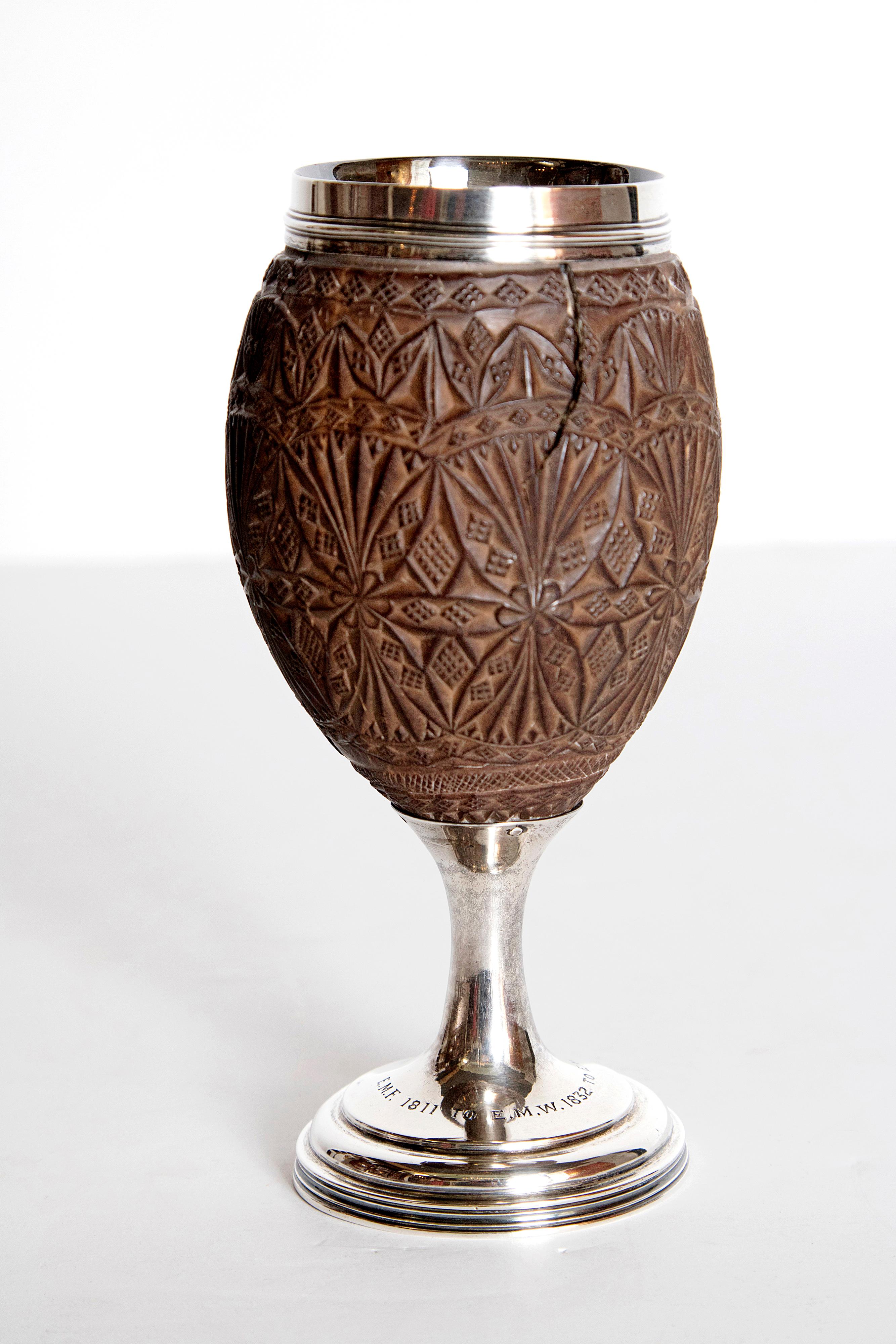 A period George III silver and coconut communion cup by English silversmith Charles Hougham (1748-1793). The coconut is carved extensively with a palm leaf pattern enclosed in crosshatched circles. The cup has a silver inner bowl and stands on a