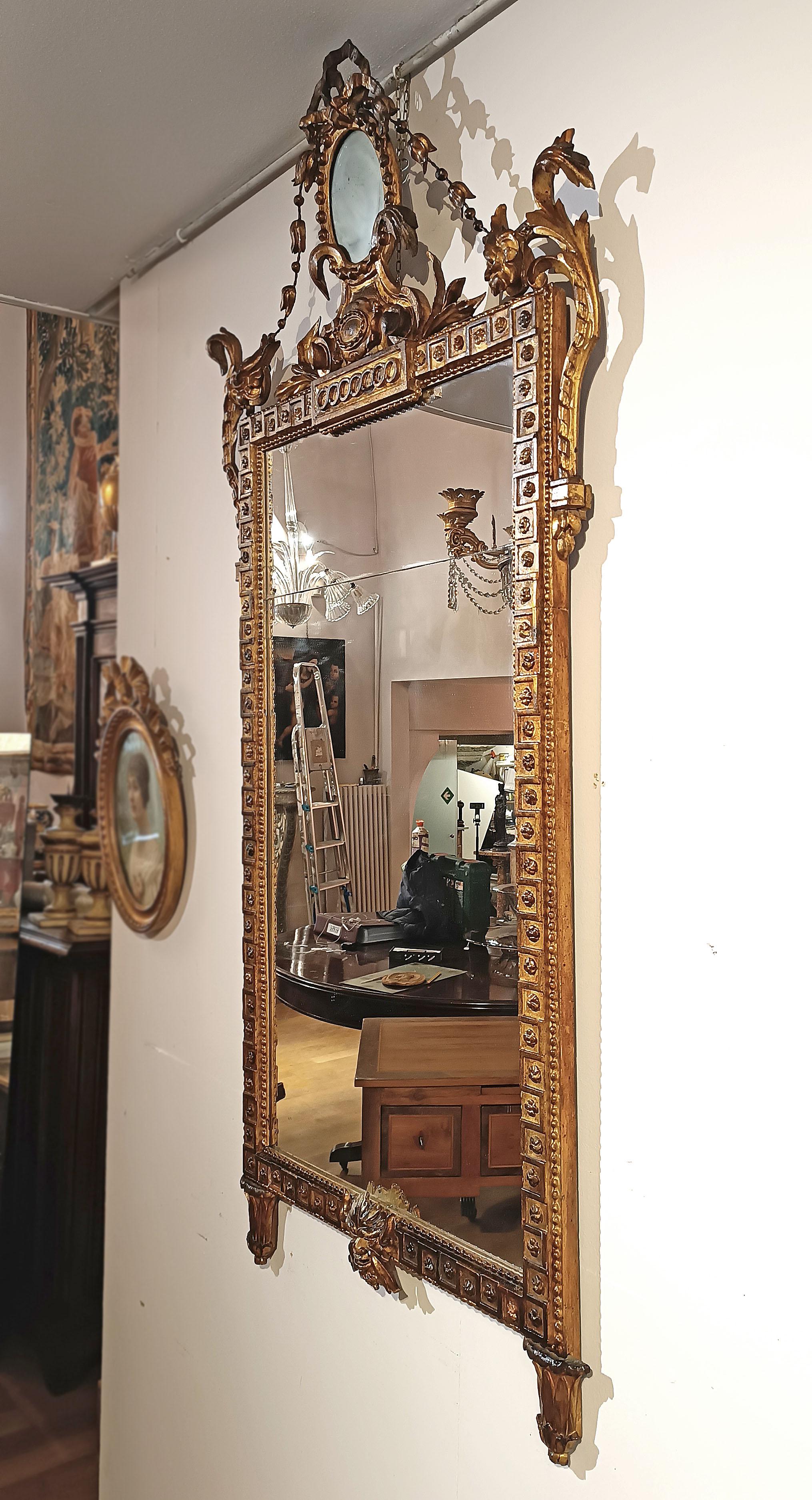 Raffinato specchio in legno intagliato e dorato con foglia d'oro puro. La cornice si distingue per la sua grande eleganza, impreziosita da raffinati motivi intagliati con disegni floreali e geometrici. Nella parte inferiore, la cornice termina con