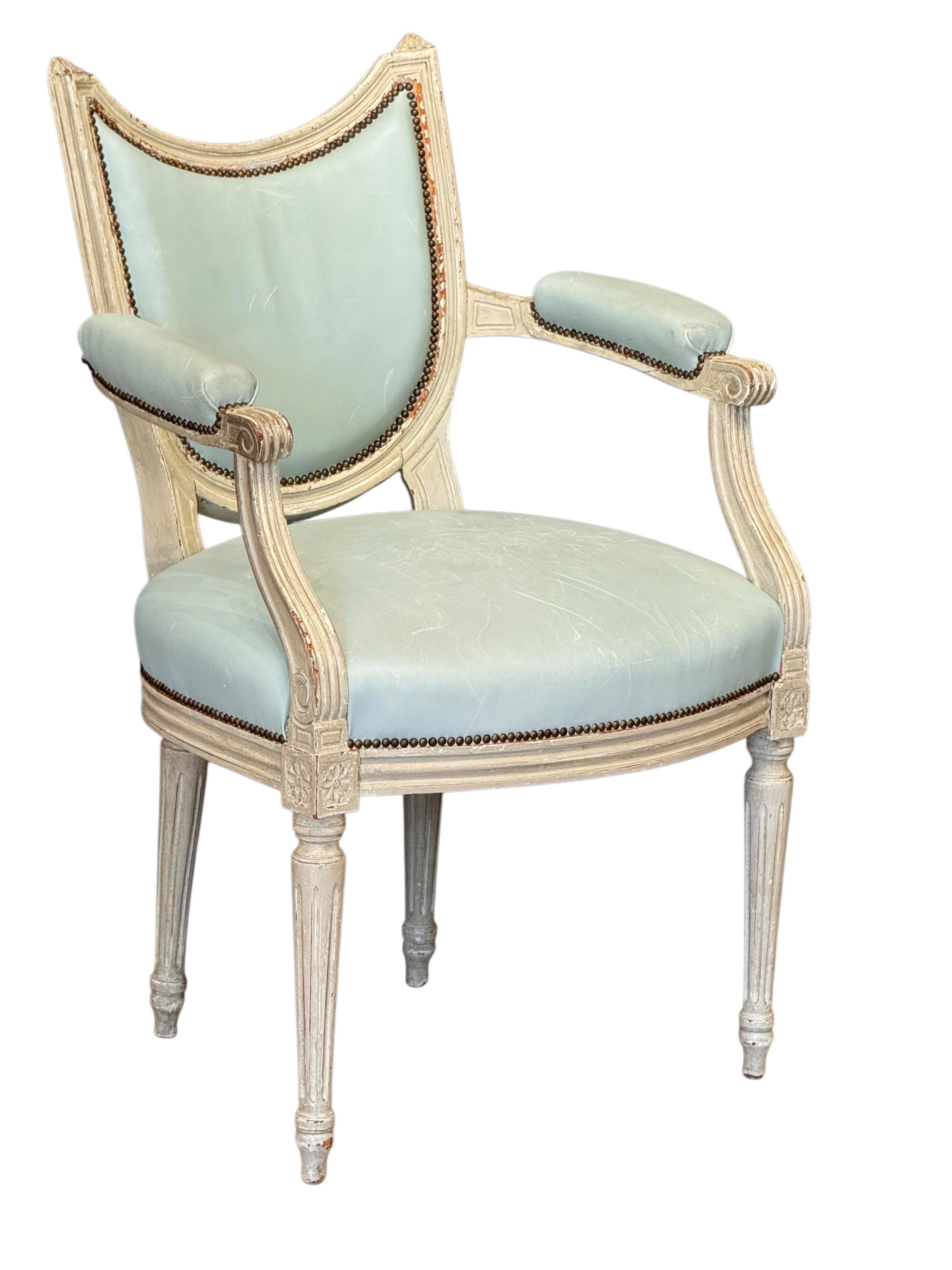 A late 18th century Swedish Gustav III armchair, white-painted with carved floral details and reeded legs. The shield-form back and seat are upholstered in soft blue leather with brass nailhead trim, showing nice age to the painted surface.
