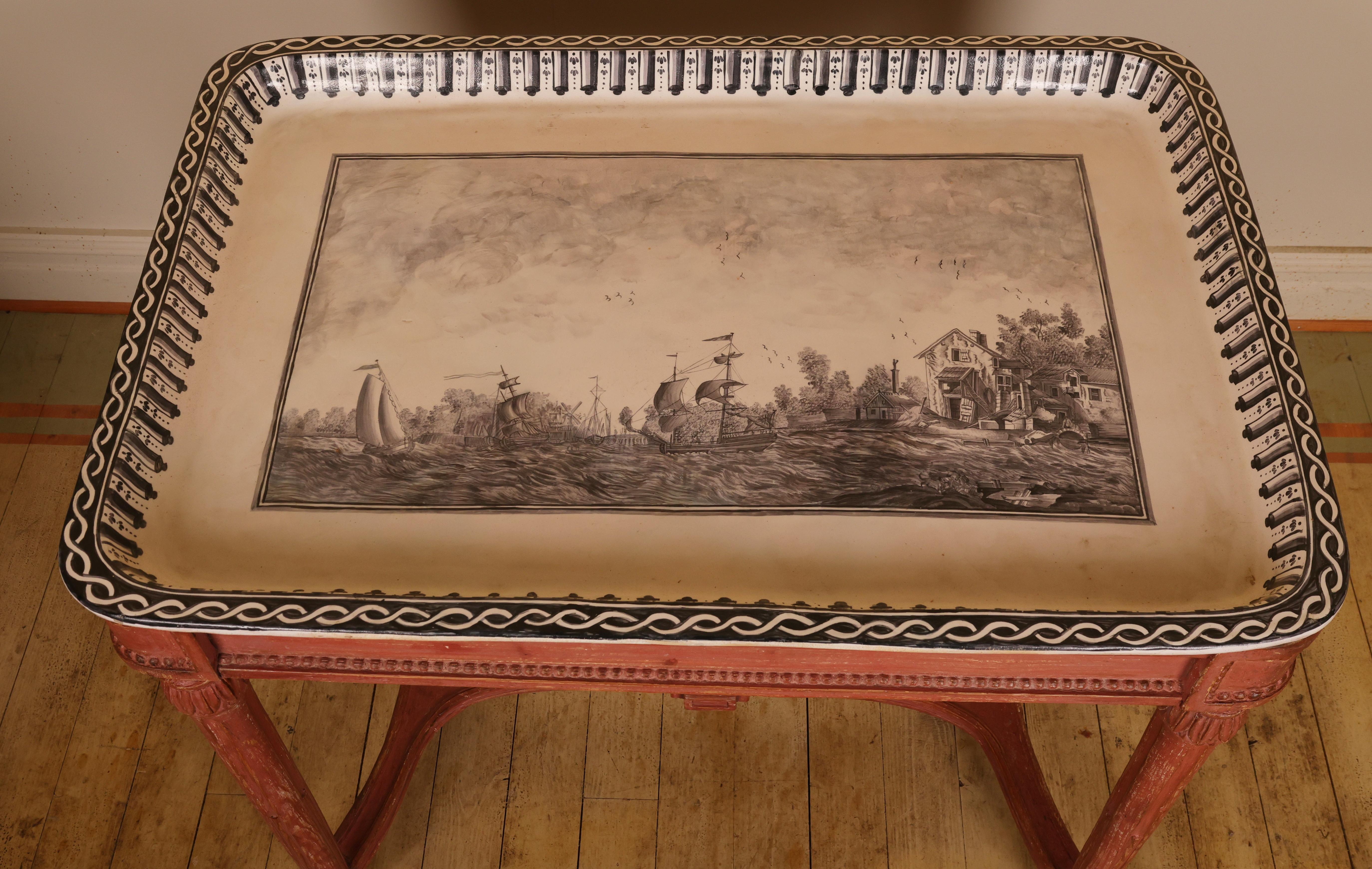 A tray table with a removable faience top made at the Rörstrand faience factory in Stockholm during the 1780s/90s. The motif depicts a naval battle in sepia tones. The top has been restored. The base is typical of the Swedish Gustavian style,
