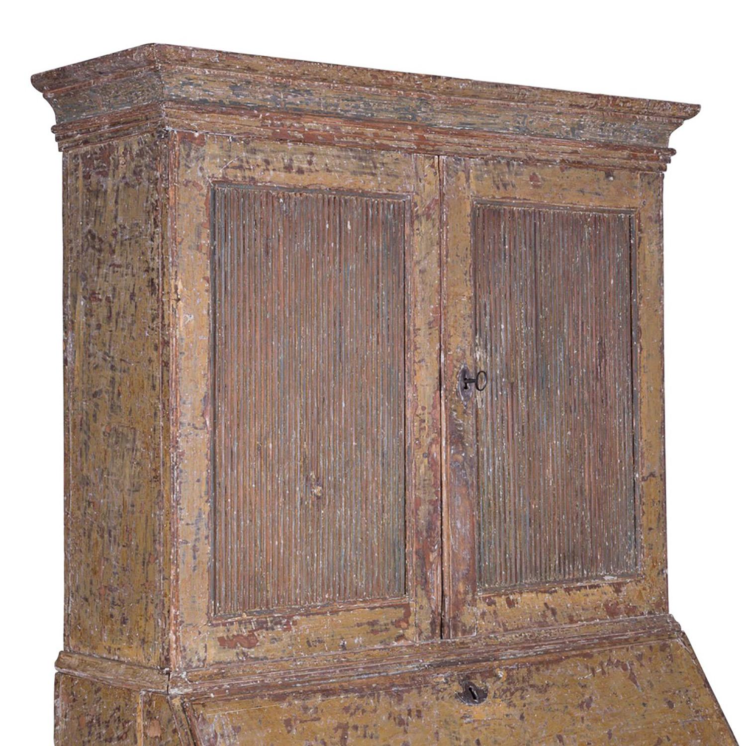 This late 18th century Gustavian secretaire was made in Berslagen in 1790 and has been scraped to secondary paint. The top two reeded front doors open to two shelves for storage, a fall front desk opens to eight drawers, and there are a further two