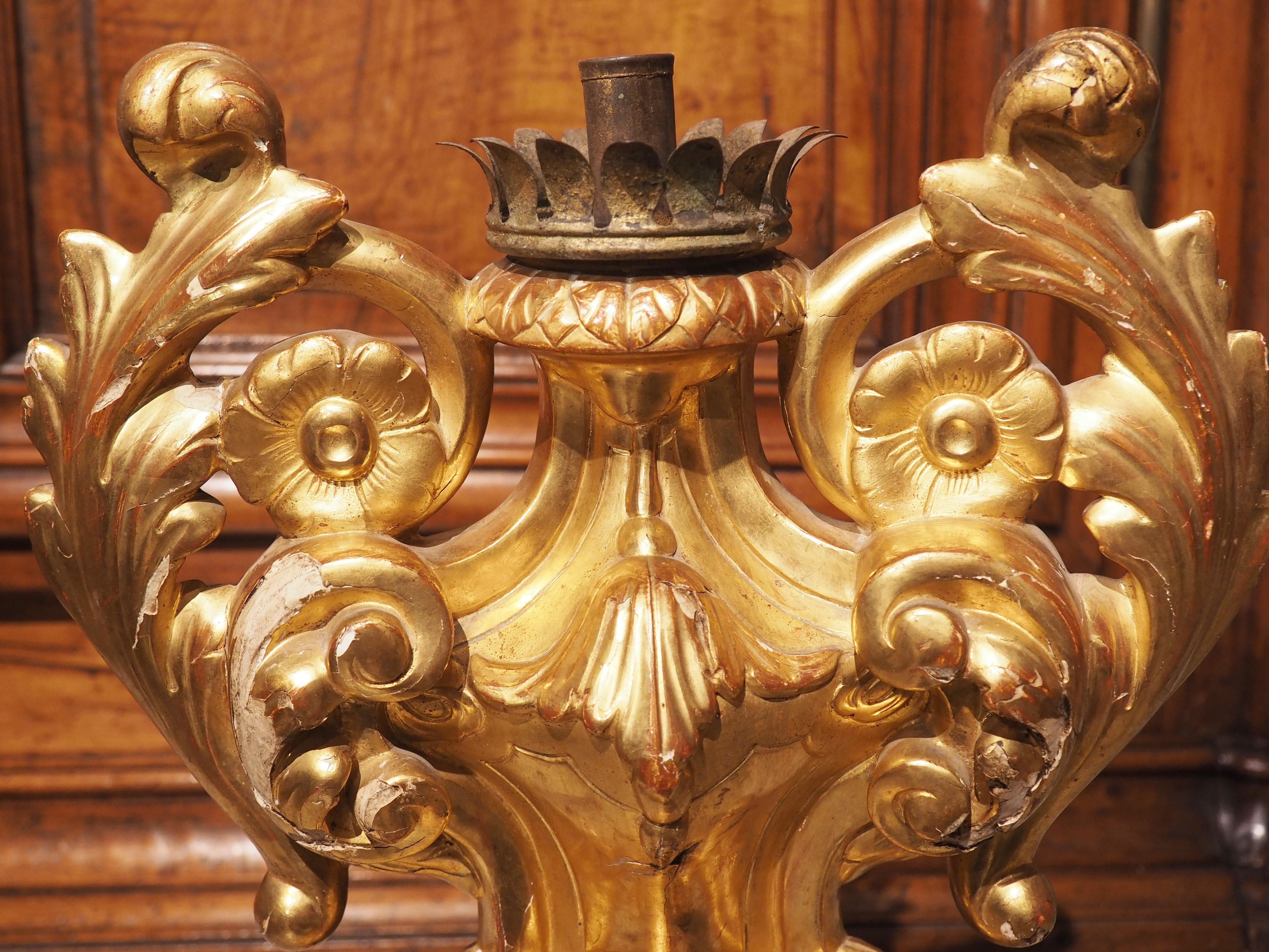 Hand-carved in the late 1700’s (the Baroque period) in Italy, this giltwood candleholder features an impressive floral and foliate rinceaux surrounding a single iron bobeche with a curled leaf edge. There is a protruding ring adorned with scalloped