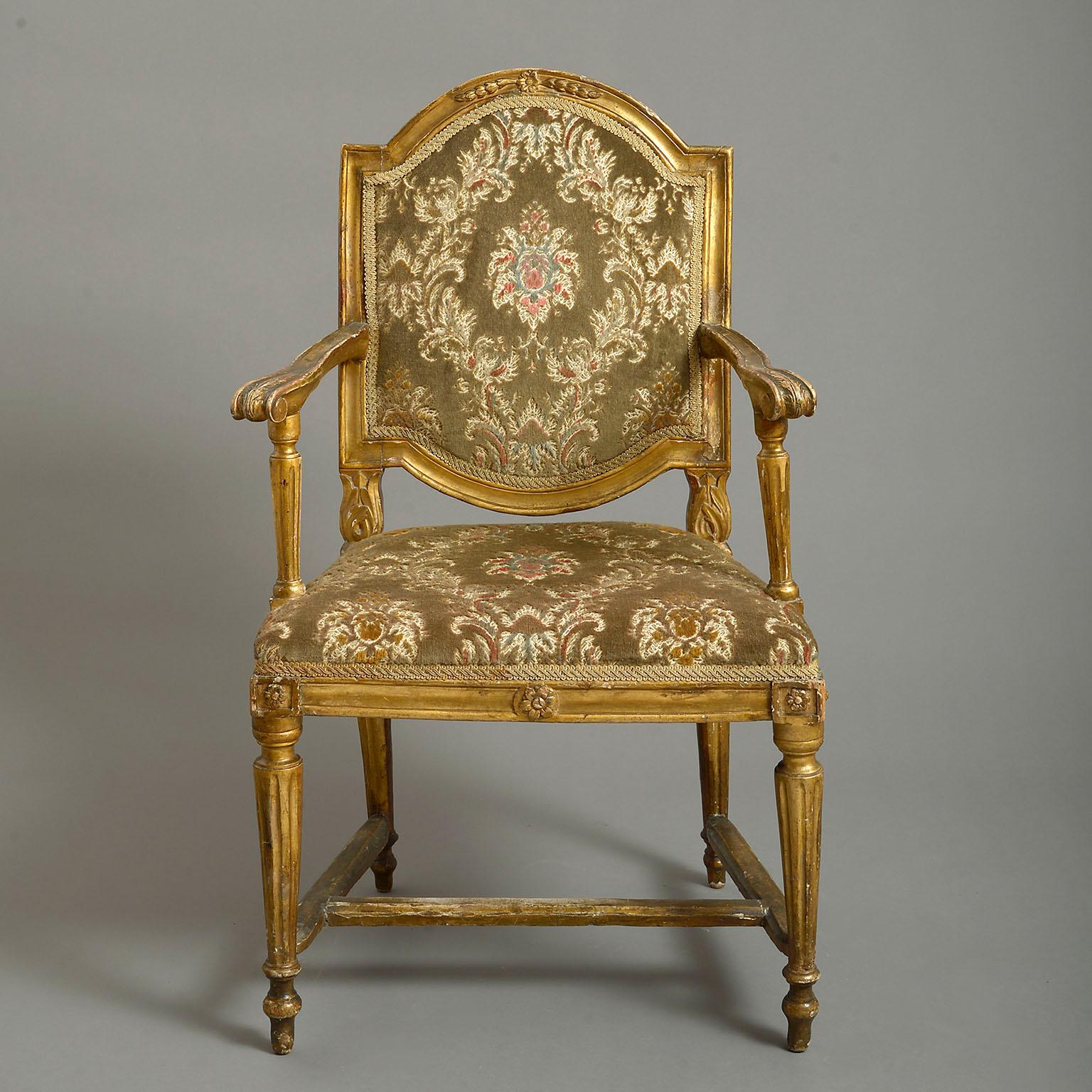 A late 18th century Italian giltwood armchair, the moulded frame carved with husks and flowerhead, and with arched stuffed back, stuffed seat and fluted tapering legs

 