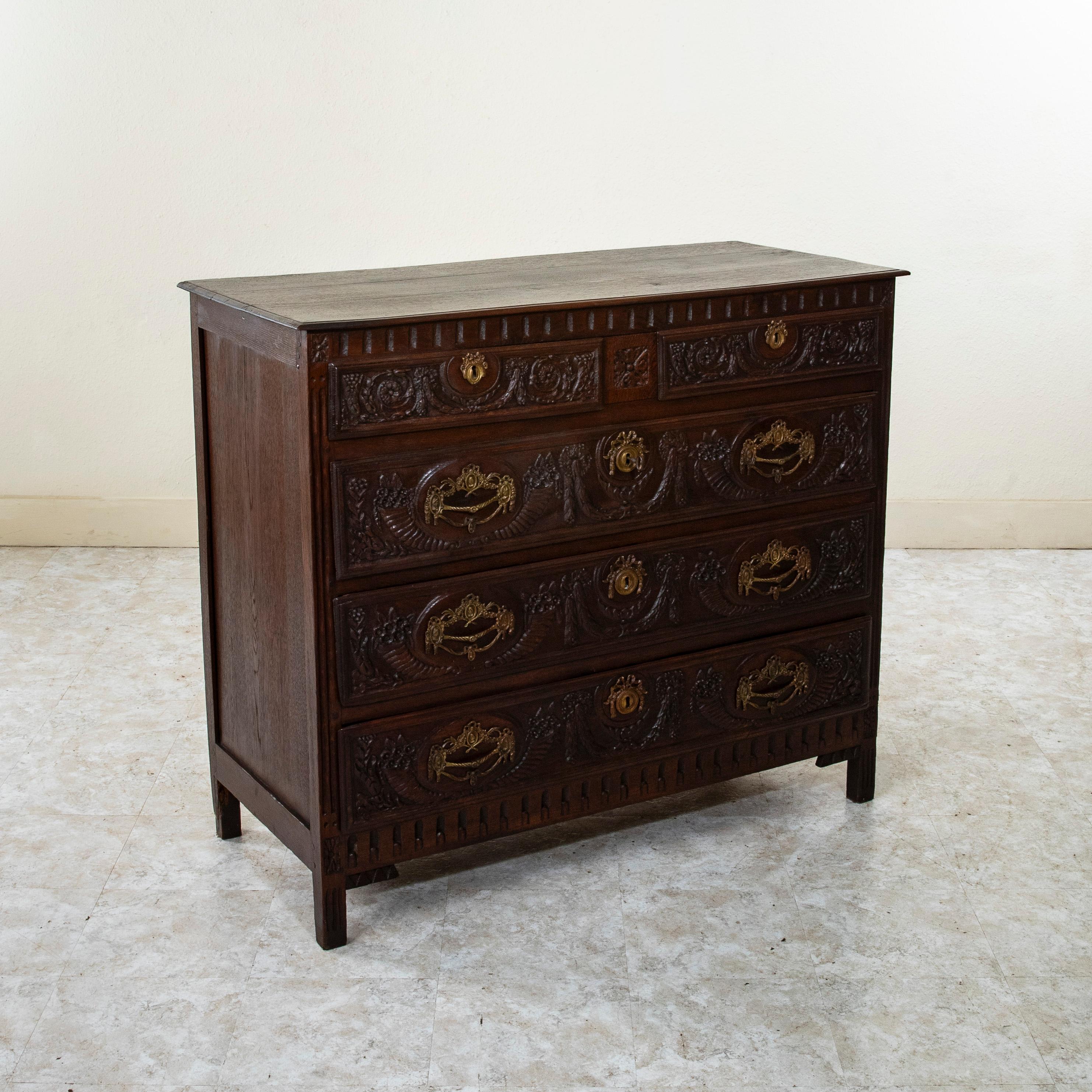 This late eighteenth century Italian oak commode or chest of drawers  features hand pegged paneled sides and drawer fronts with hand carvings of garlands and cornucopia. Its three drawers are each appointed with their original bronze drawer pulls