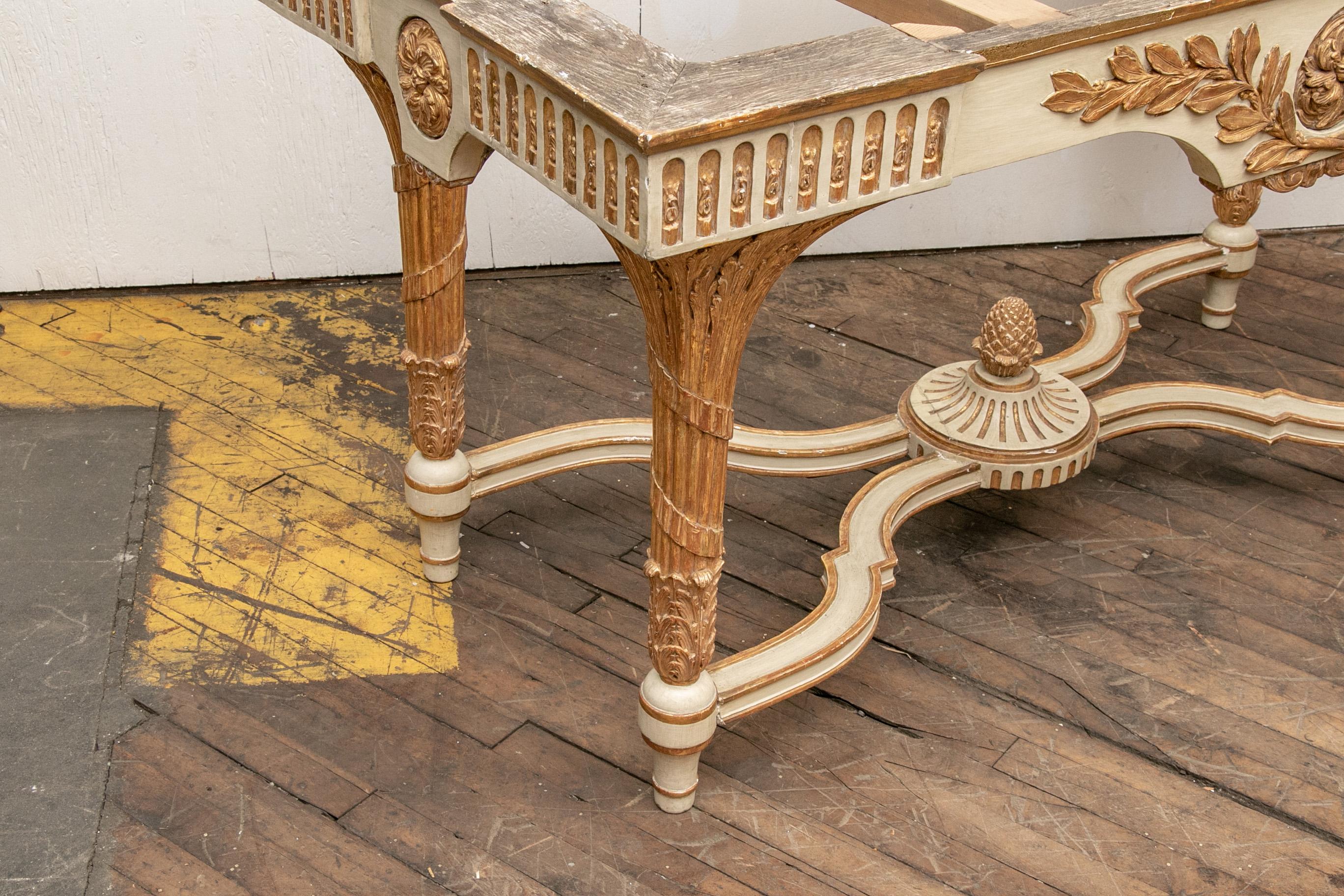 The table in cream paint with carved and gilt details- the frieze with laurel leaf spray and rosette, rosettes and leafy bars on the sides. Raised on heavy carved and leafy gilt legs with ribbon twists. A double shaped stretcher with large centre