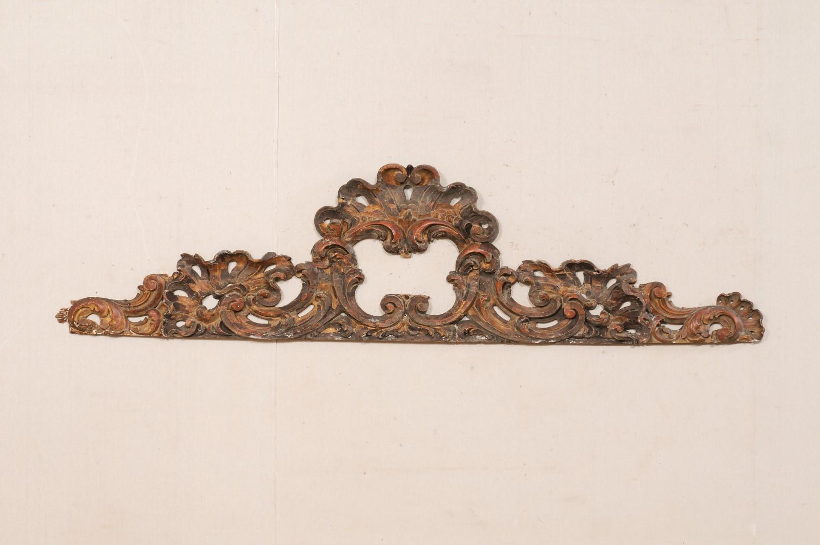 An Italian carved-wood pediment fragment, with its original finish, from the turn of the 18th and 19th century. This antique wall ornament from Italy, with it's horizontal span of over 6.75 feet in length, has been hand-carved in a swirling
