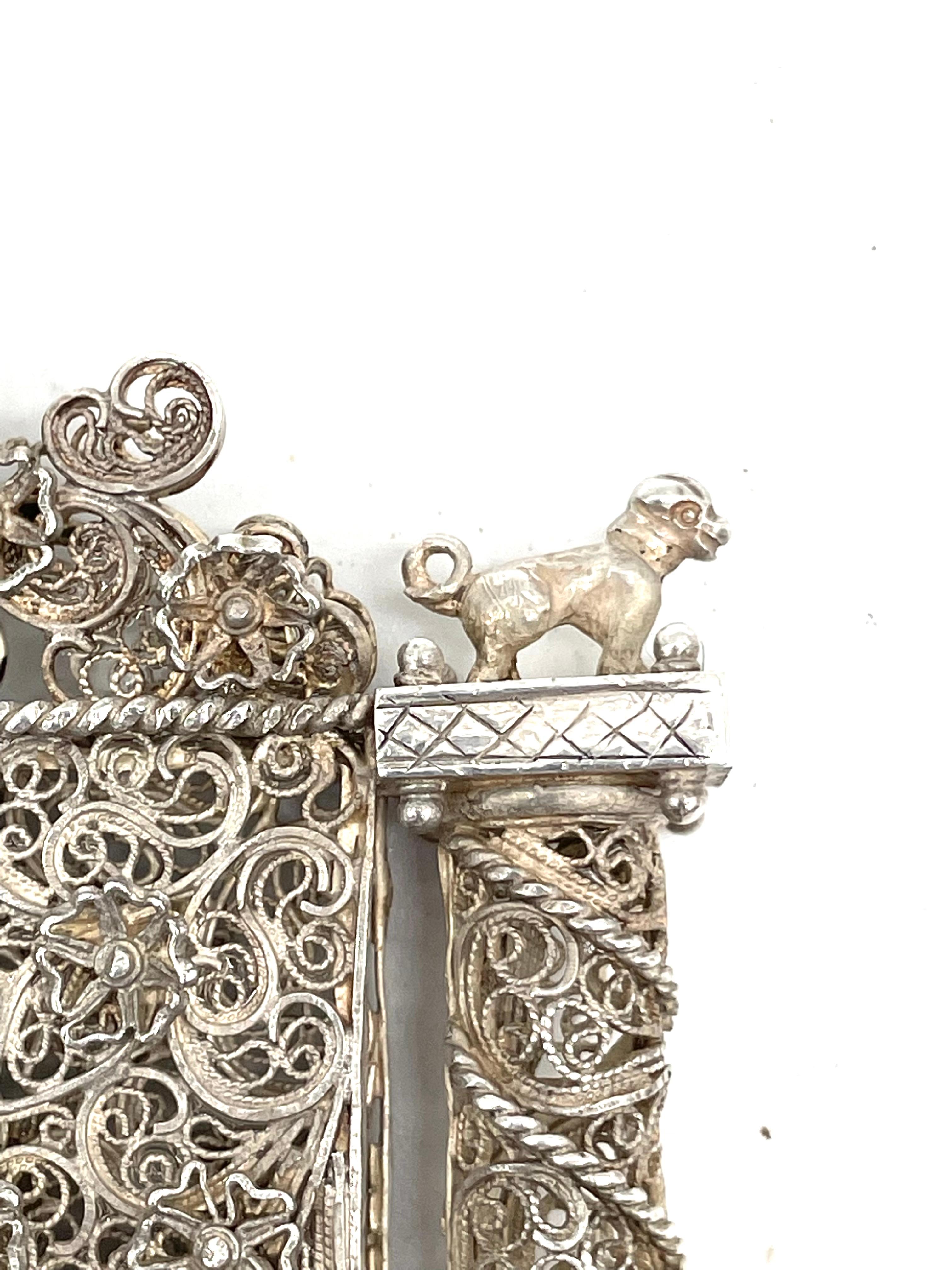 Handmade amulet with silver and silver filigree. A rectangular shape, flanked by two separated baroque columns topped by collared hounds, applied with flower-heads and centered on both sides by a shield with applied letters G-d.

Every item in