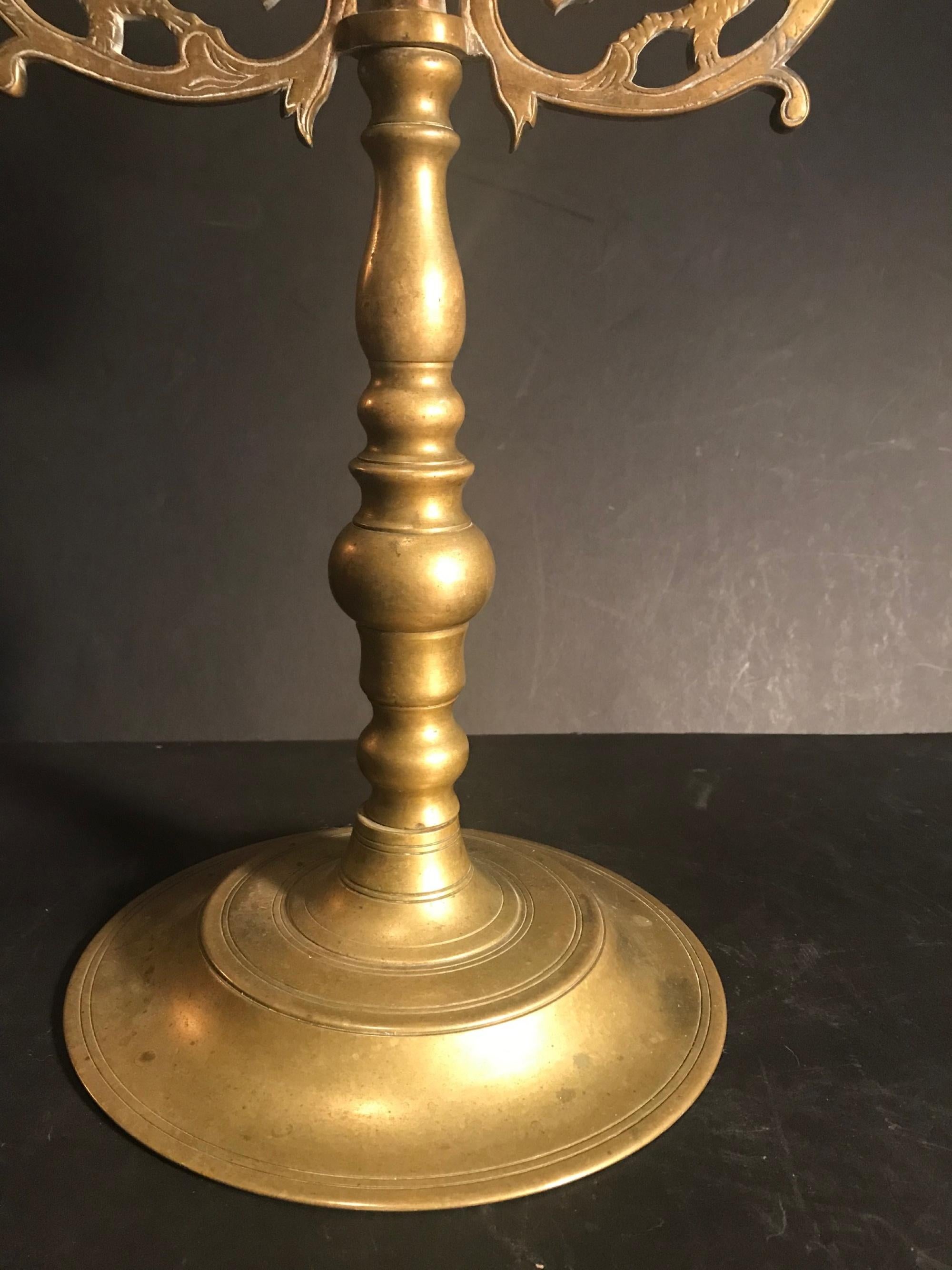 This glorious brass four candle candelabra is set on a heavy round base with a turned stem. The upper portion is decorated with lions facing each other. Engraved details outline and embellish the lion figures. Centered at the top is a finial of the