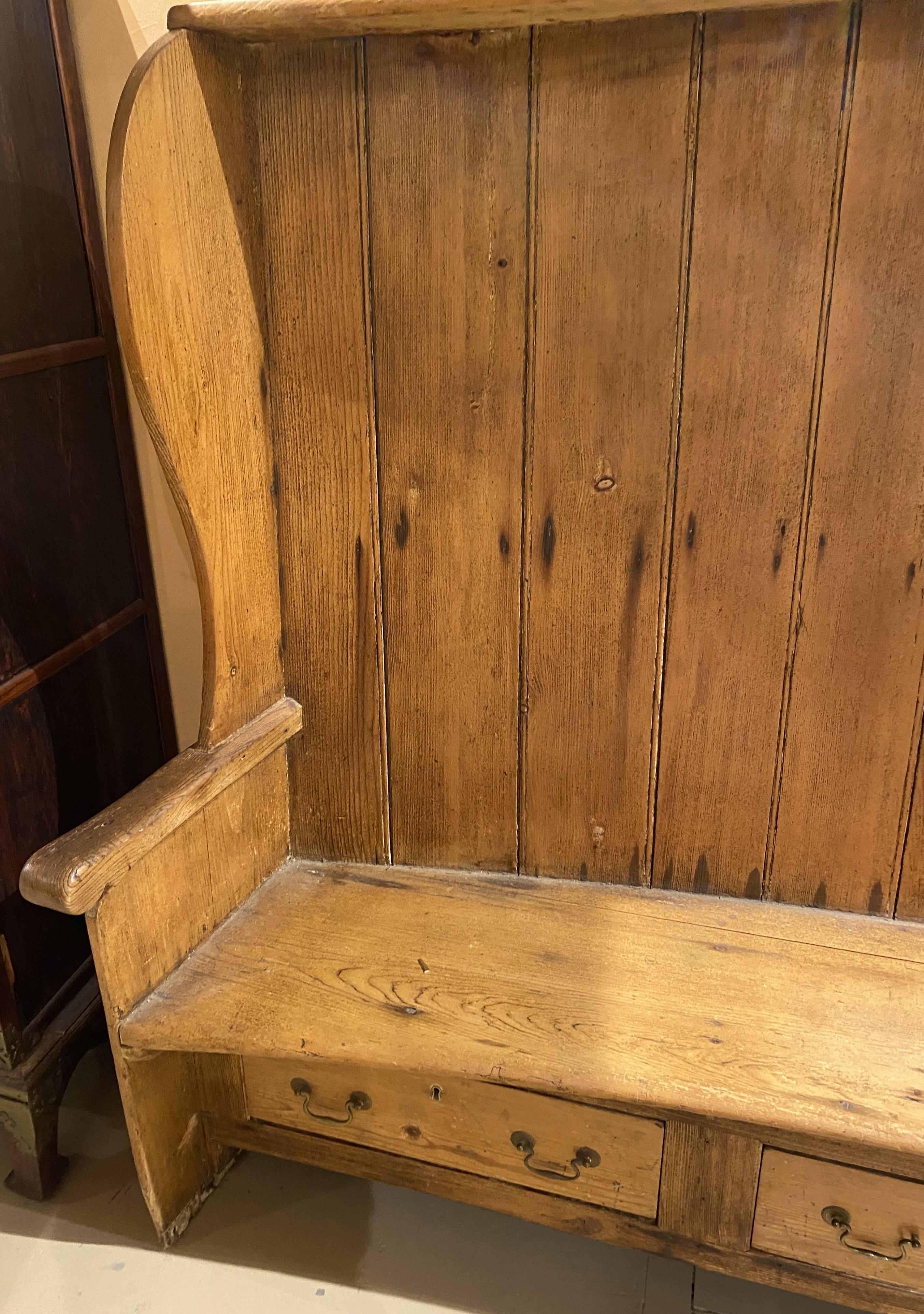 A great form large pine bow back settle bench with tongue and groove back, carved arms, conforming seat, and three fitted drawers. English in origin, dating to the late 18th century, in good overall condition, with some molding losses and water