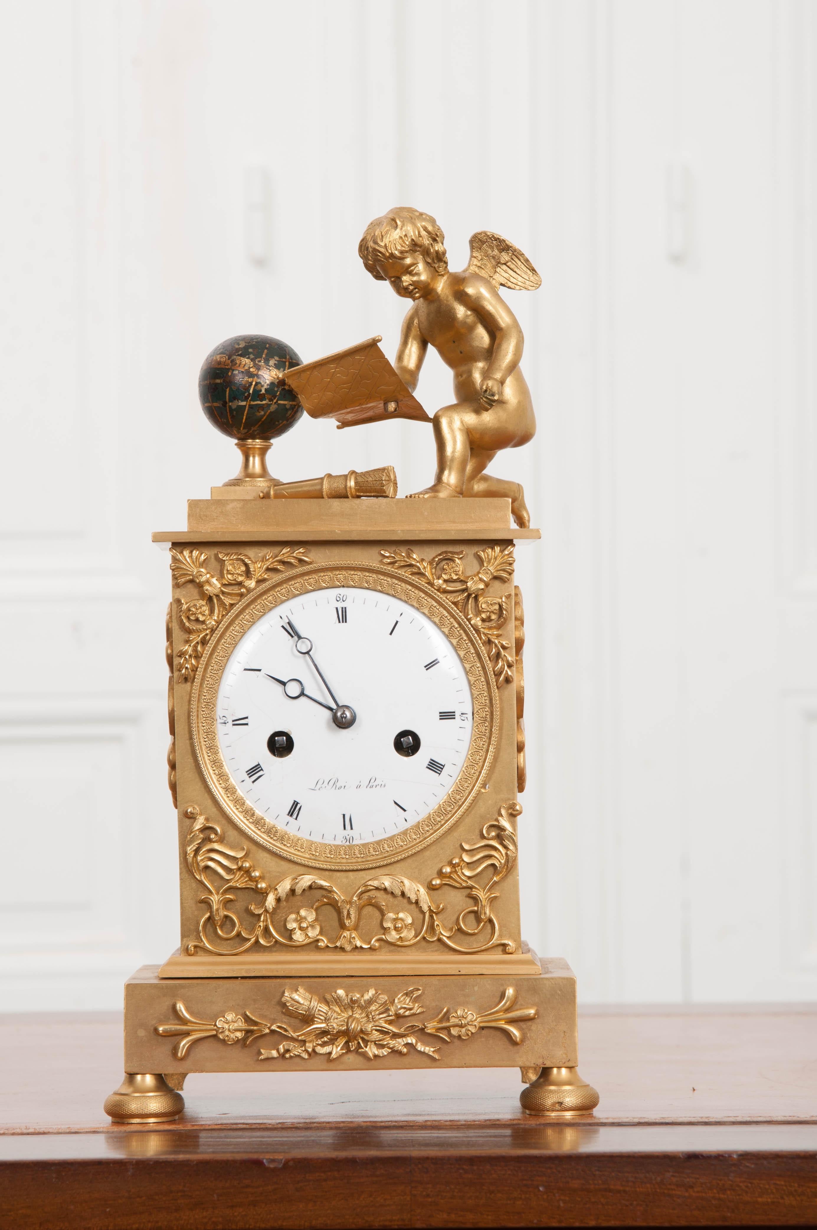 This exquisite fire-gilded bronze mantel clock was made in France, circa 1790-1800. Depicting the Arts in Astronomy, it features a winged cherub reading from a scroll with a painted bronze globe and telescope nearby. The delicate hand painted enamel