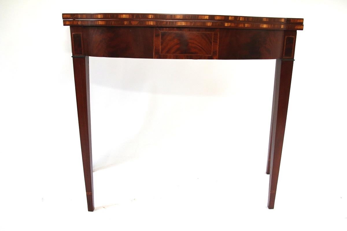 Hepplewhite semi-elliptical carved mahogany card table with exotic wood inlay around table edge, cuff inlay on legs, and central cartouche with flame inlay. Hinged swing leg to support table when open. Signed underneath Thomas Pinkhamton.

Salem