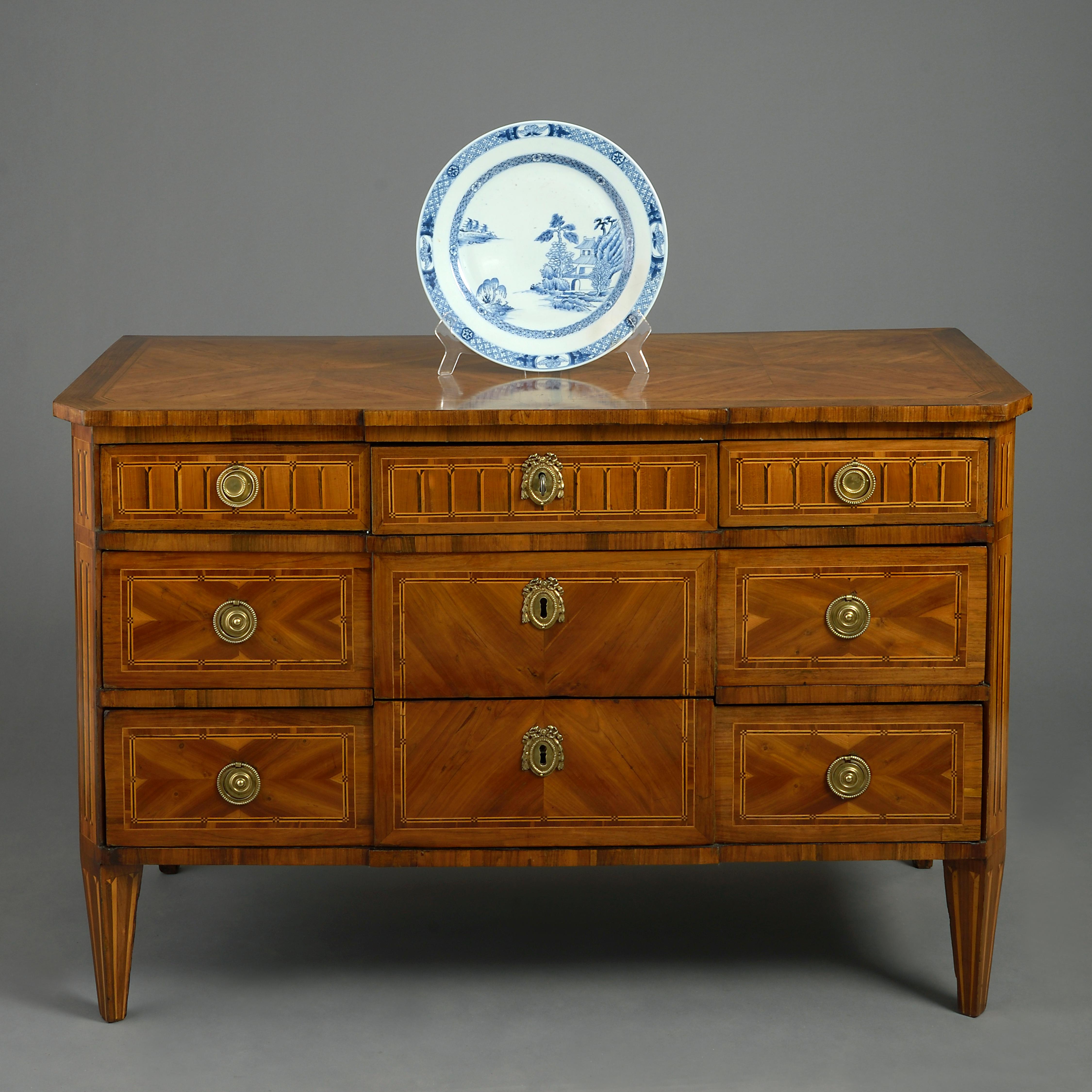 A fine late 18th century parquetry commode veneered throughout in amaranth, walnut, ebony and boxwood, the overhanging geometric top above a carcass with broken front of three drawers with stringing and inlay, all raised on square tapering feet of
