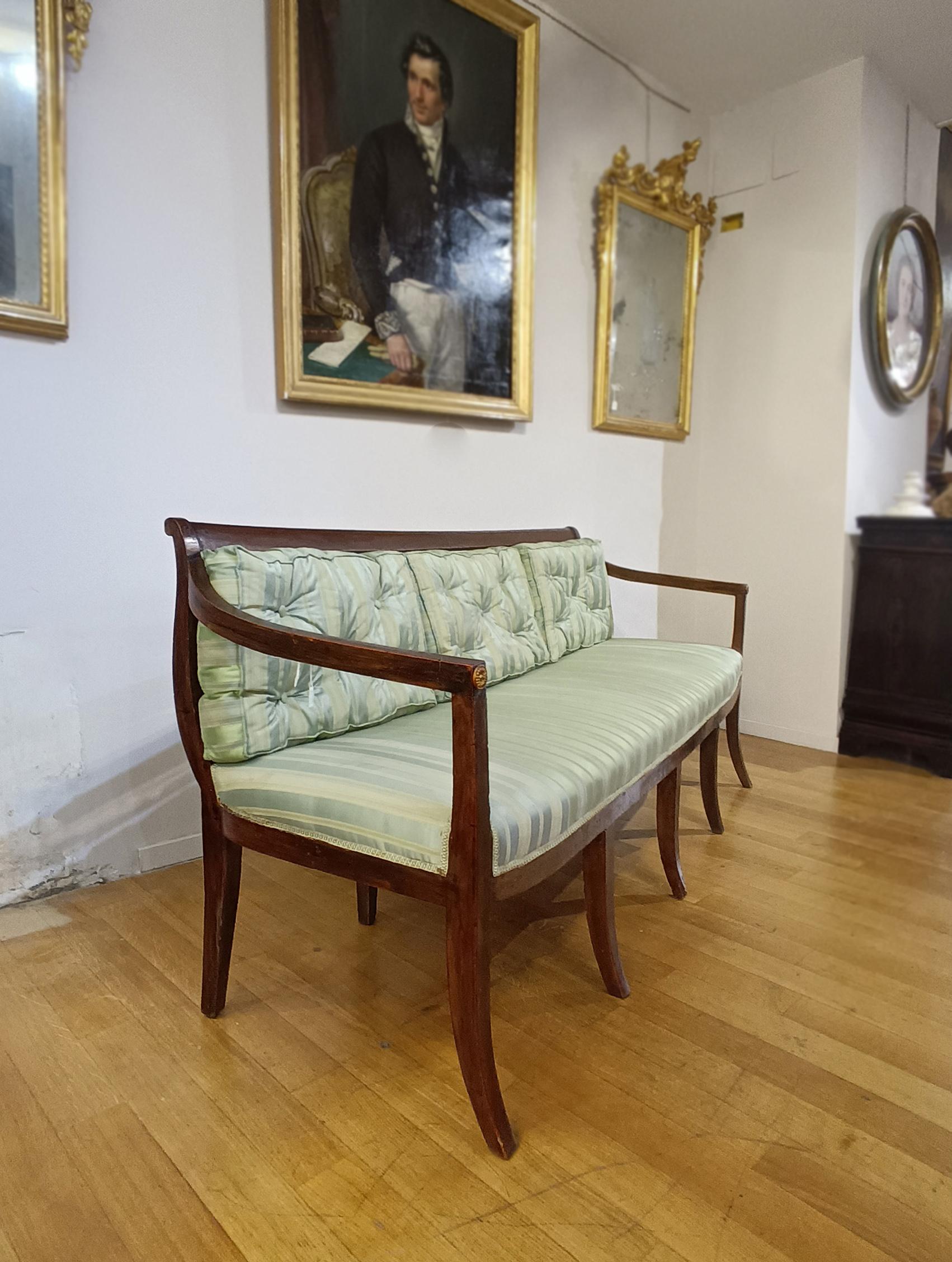 Elegant hand-carved solid walnut sofa. Its shape is distinguished by the wavy lines of the backrest and armrests, while the legs, characterised by a slightly curved truncated pyramid shape, recall the style of the Directoire period. To further