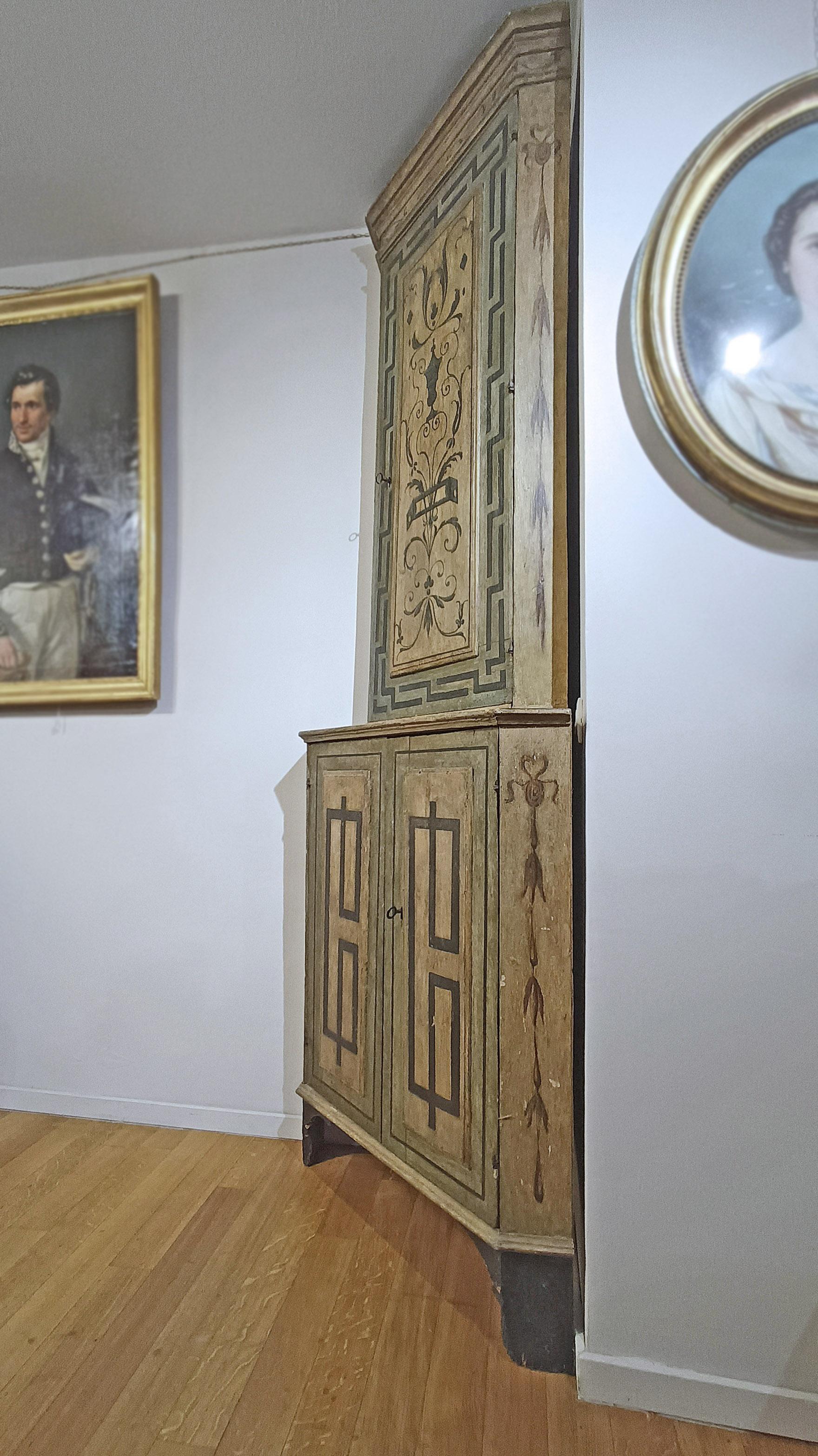 Beautiful fir wood corner cabinet, painted in tempera and finished with wax. The lower section features bracket feet and two lockable doors, containing two shelves ideal for storing objects. The upper, taller section consists of a single door that