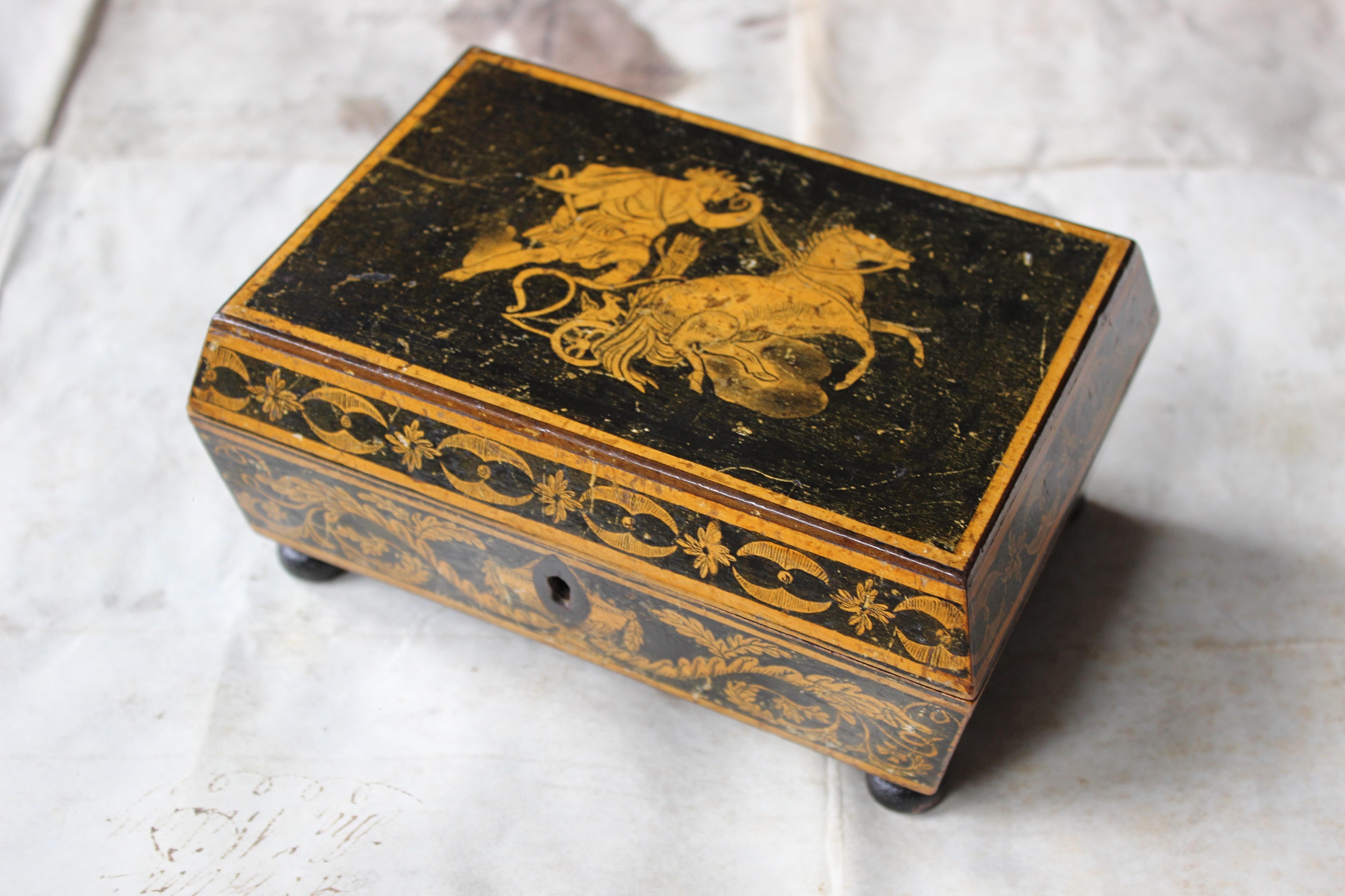 A George III penwork sarcophagus work box with hinged lid decorated with a chariot, the side with Neo-Classical devices.

Age related abrasions and knocks later replacement ebonised bun feet. 

17/7.5/12cm  