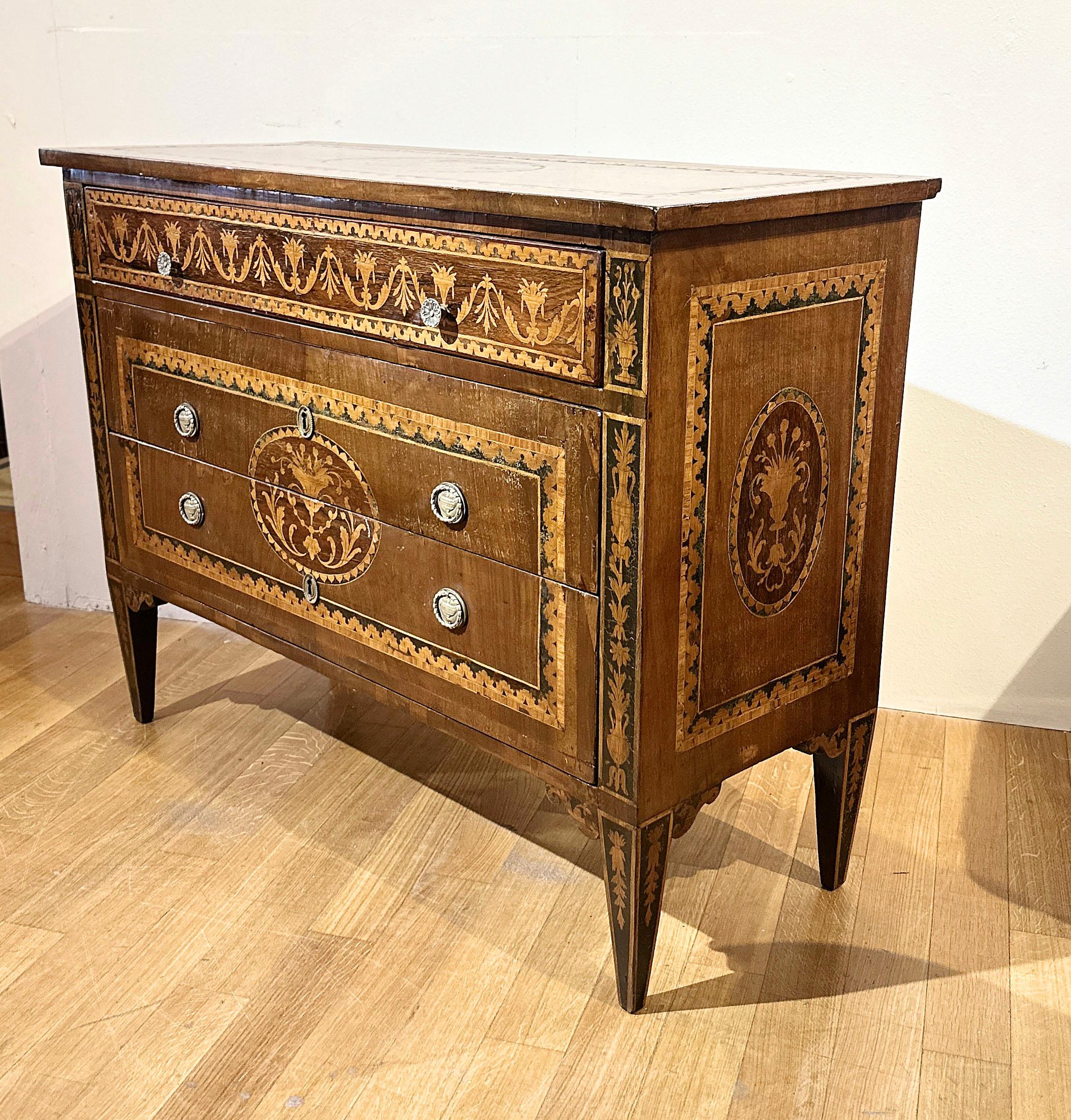 Sontuoso cassettone rivestito in noce, impreziosito da intarsi in legno di frutta e pastiglia, una tecnica tipica della scuola ebanistica lombarda. La cassettiera presenta gambe tronco-piramidali, caratteristiche dell'epoca, e una forma lineare ed