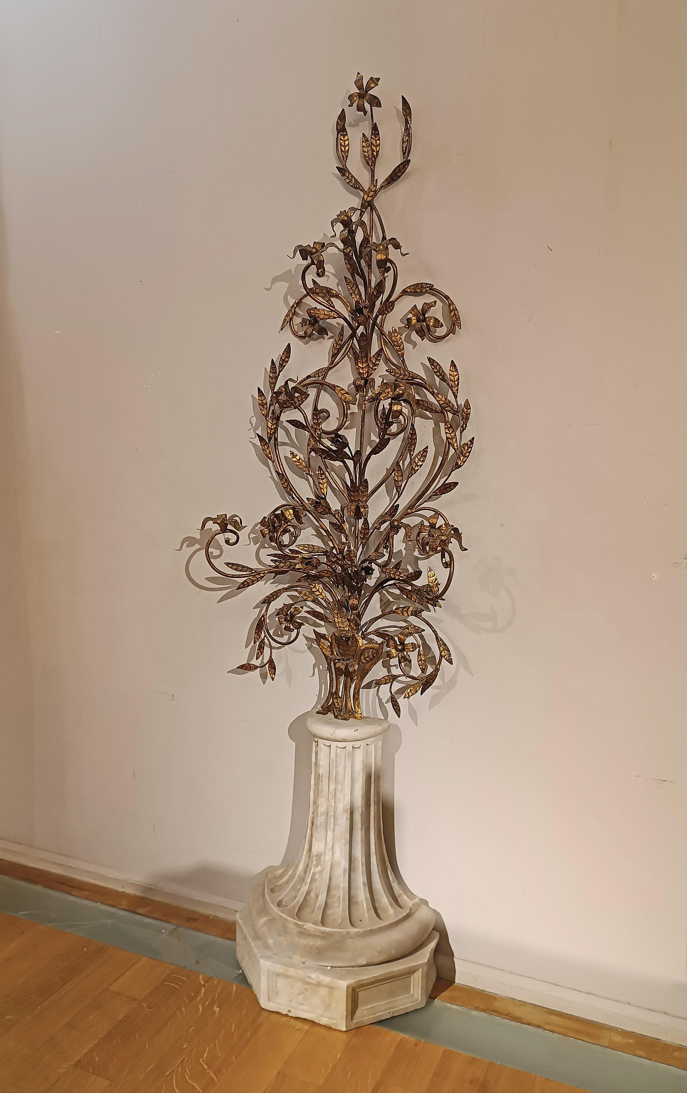 Elegant ornamental frieze in wrought iron and hand-forged, finely gilded and embellished with floral motifs that enhance its elegance. The base is made of white Carrara marble, carved, turned and pilastered to simulate a column base. This ornamental