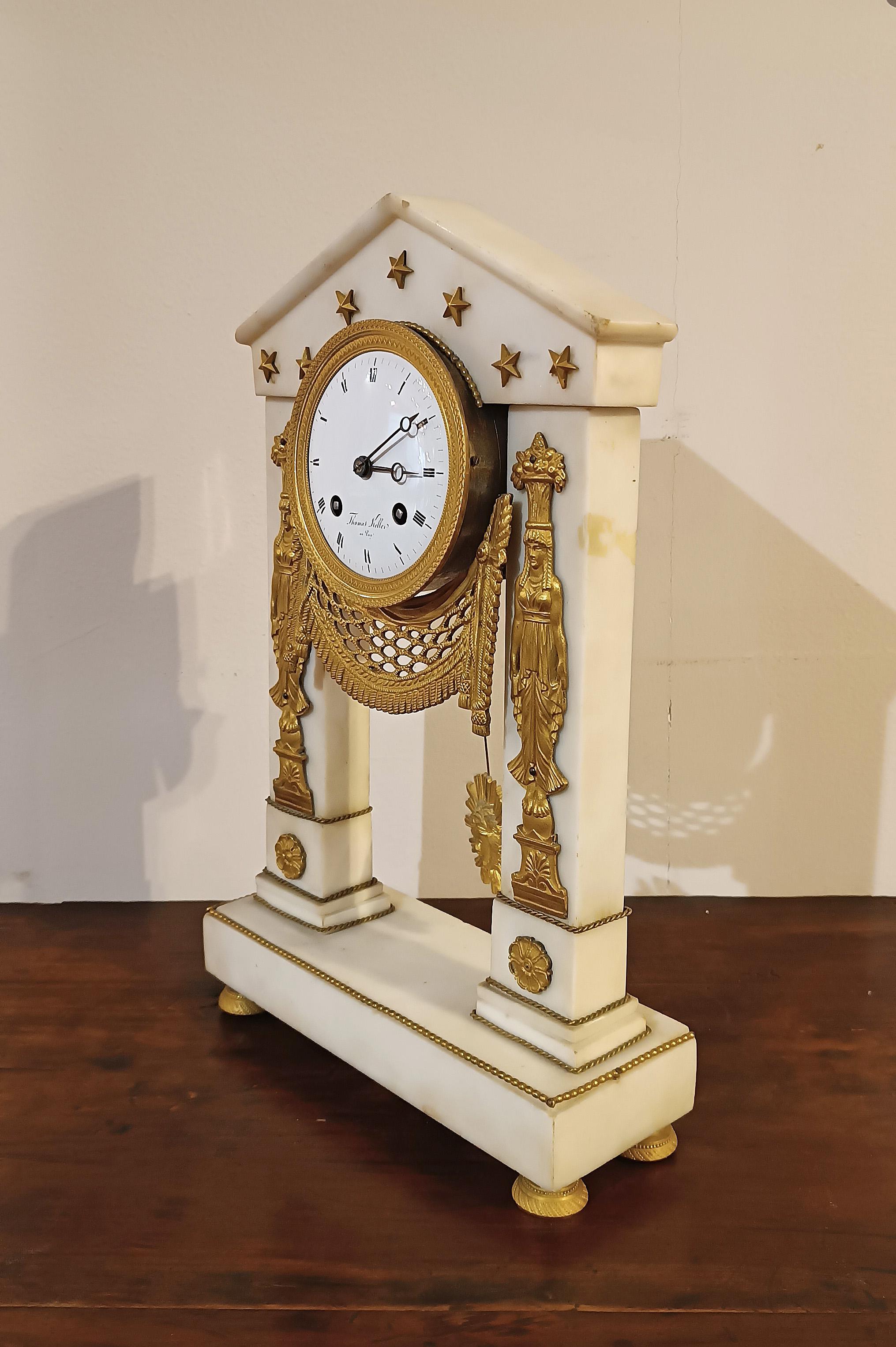 Elegant “tempietto” clock in white marble with gilded bronze finishes. The clock features a rectangular base, embellished with two columns and a temple top. The finish is embellished with classically inspired gilded bronze details, such as caryatids
