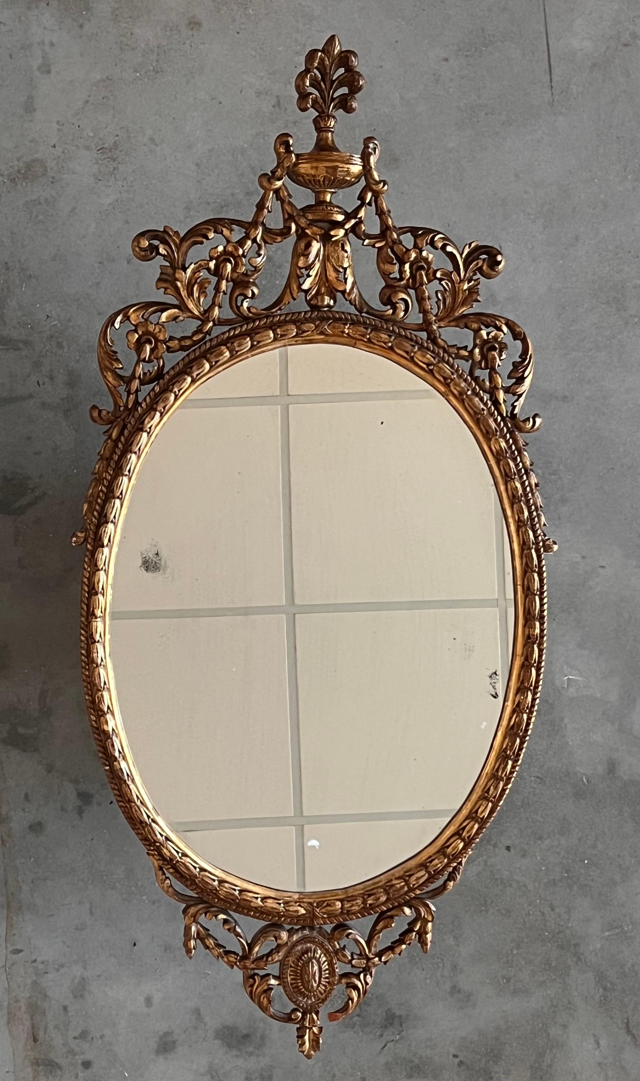 A superb 18th century oval gilt mirror with raised superstructure of a classical urn draped with tied husks, above foliate scrolls which continue down each side, ending in further tied tails of husks. Resting on a faux mantle with draped foliage and