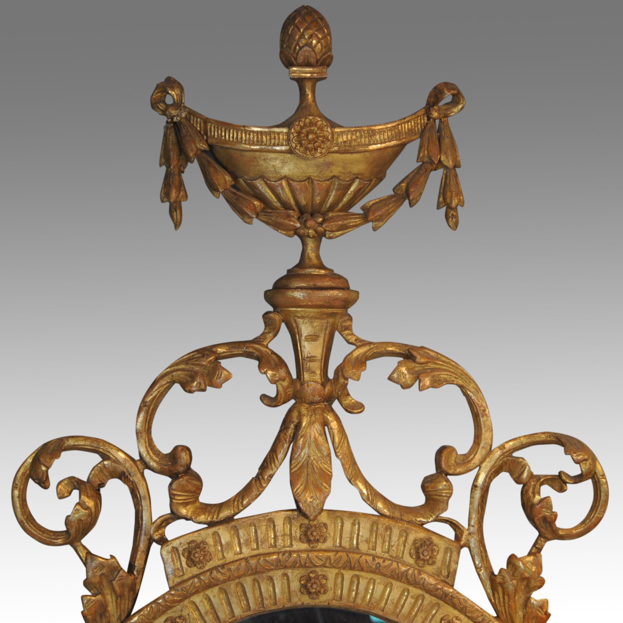 Superbe miroir ovale doré du XVIIIe siècle, dont la superstructure en relief représente une urne classique drapée de cosses liées, au-dessus de rinceaux feuillus qui se poursuivent de chaque côté, se terminant par d'autres queues de cosses liées.