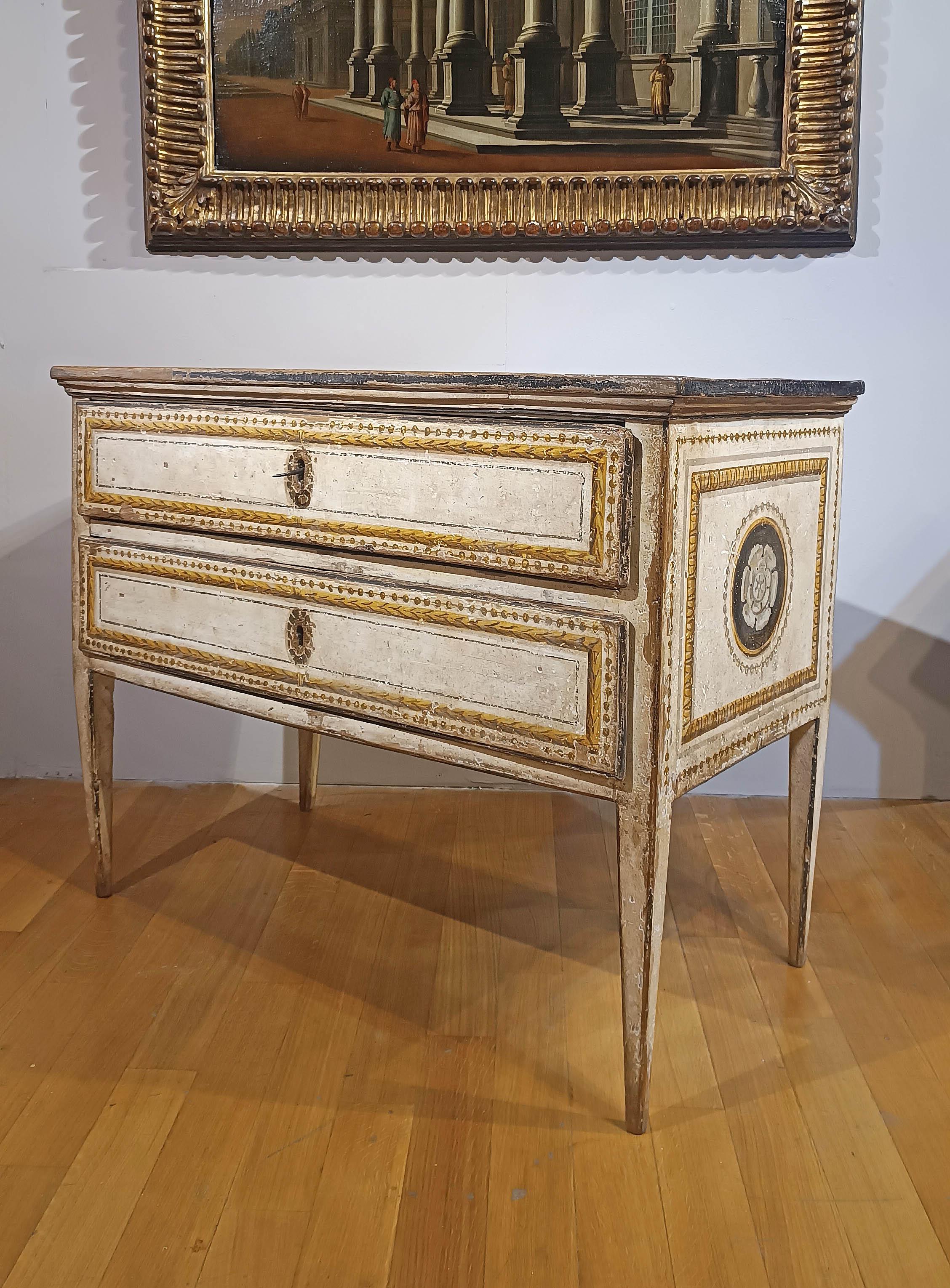 Élégante et ancienne commode en peuplier peinte à la détrempe en or, brun et blanc. La structure se distingue par ses pieds pyramidaux tronqués et son sommet décoré d'une peinture en faux marbre, ce qui renforce encore son raffinement. Les