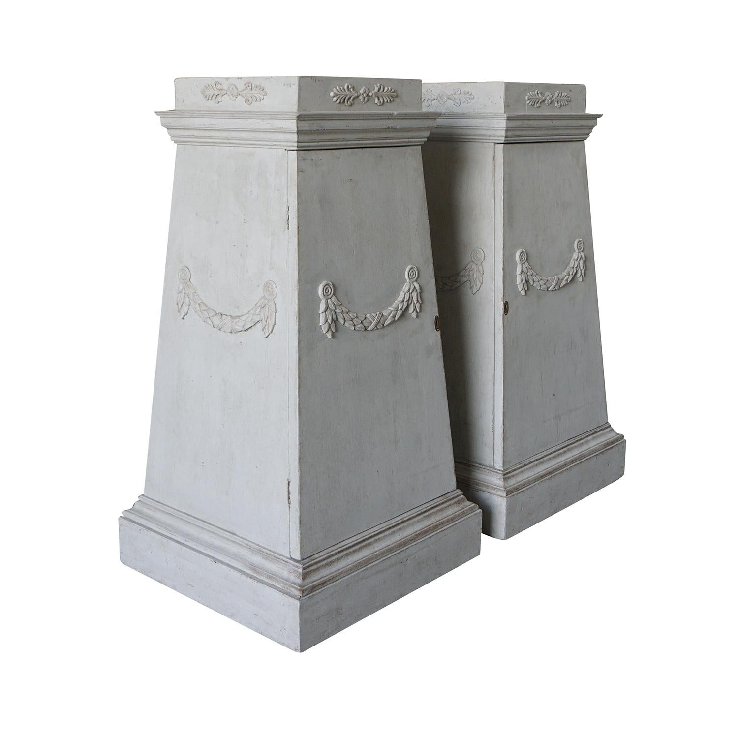 A white-grey, antique pair of Swedish Gustavian pedestals, cabinets made of light-grey painted Pinewood with carved garlands. The hand carved Scandinavian commodes are in good condition, detailed in the Neoclassical Greek style with their original