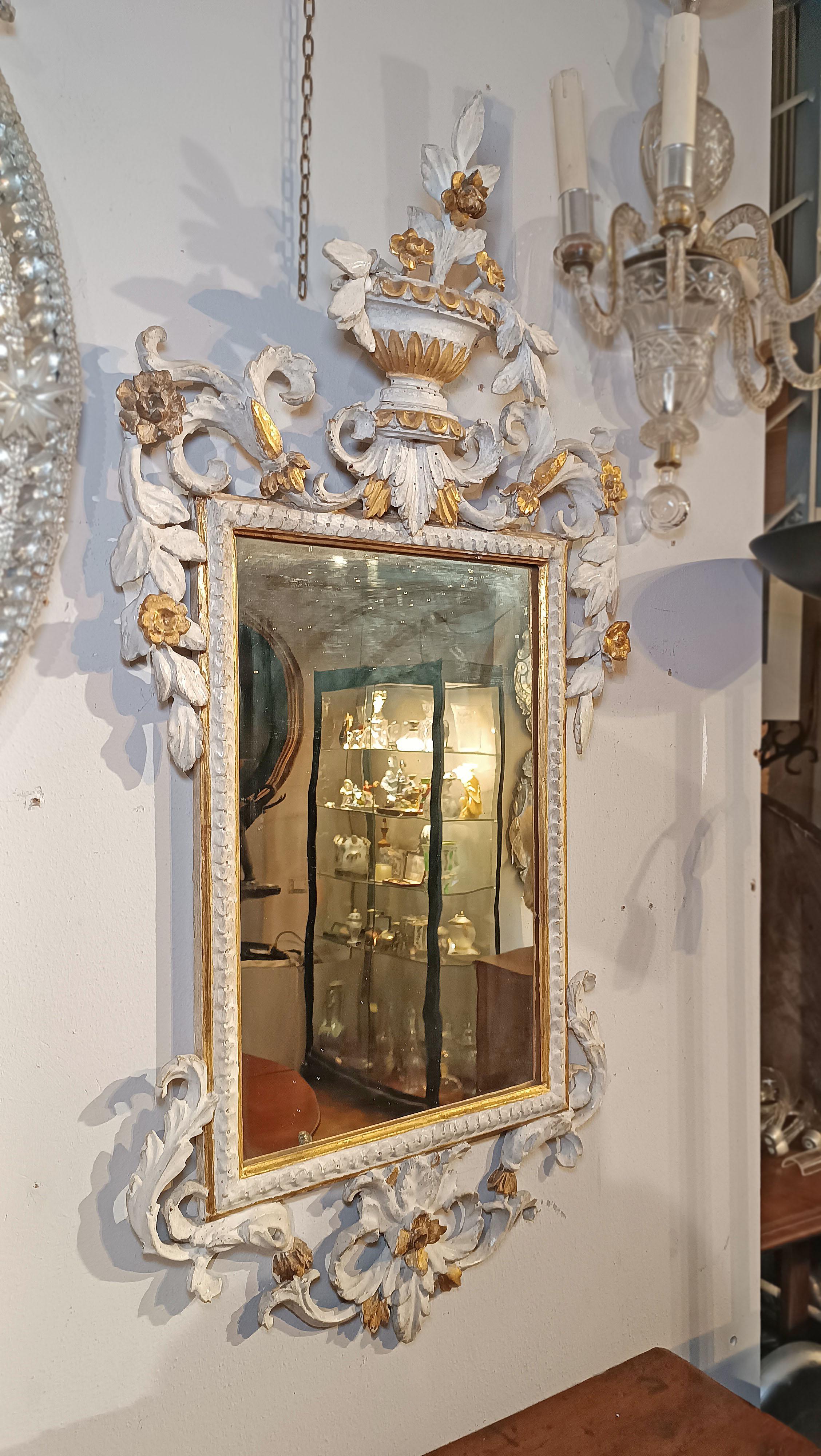 Elegant pair of small mirrors, made of finely carved and lacquered Swiss pine wood with lean tempera and partly embellished with decorations in pure gold leaf. The frames of the mirrors are enriched with vegetal scrolls, continuing also on the
