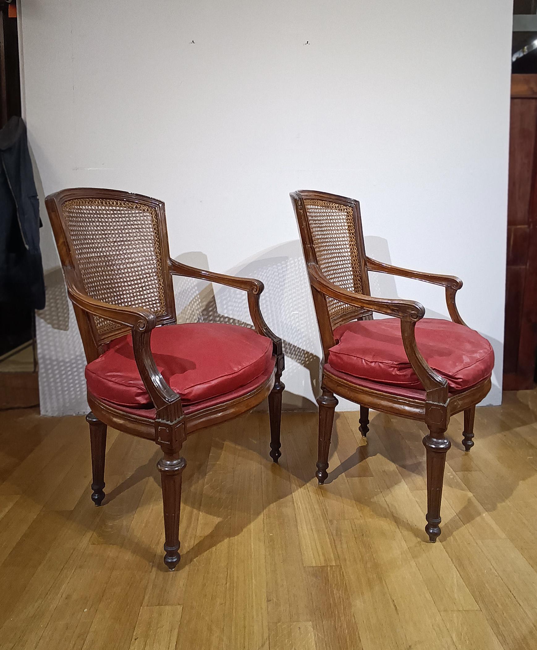 An elegant pair of armchairs crafted from solid walnut, finely carved with exquisite details. The armchairs are distinguished by their expertly turned truncated pyramid legs, curved armrests, and a backrest embellished with a geometric cane weave,
