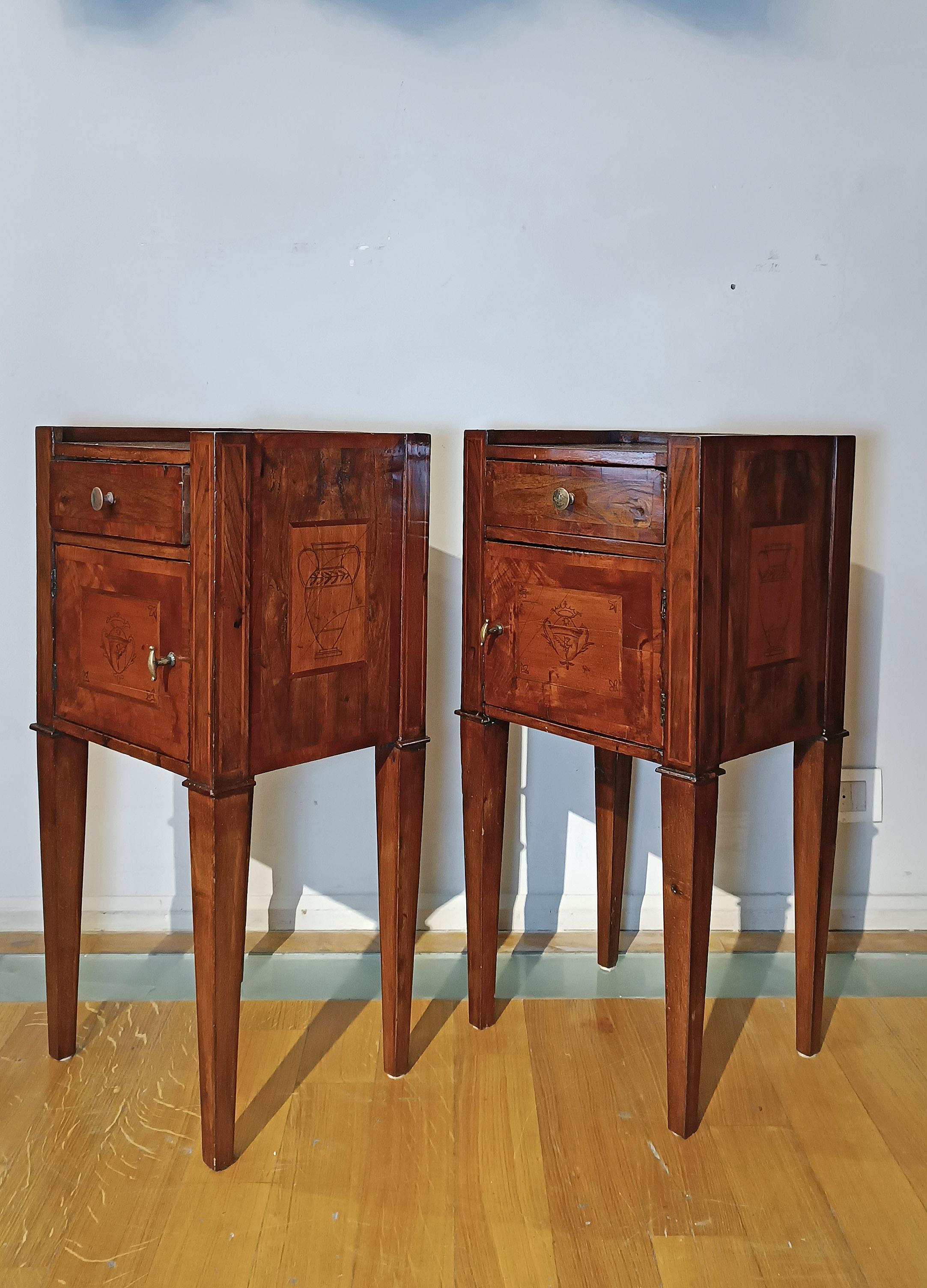 Élégante paire de tables de chevet en noyer massif, enrichie d'incrustations de cerisier raffinées. Ces détails, caractéristiques de la période néoclassique, sont réalisés avec la technique du graffito. Un blason stylisé se détache sur le devant,