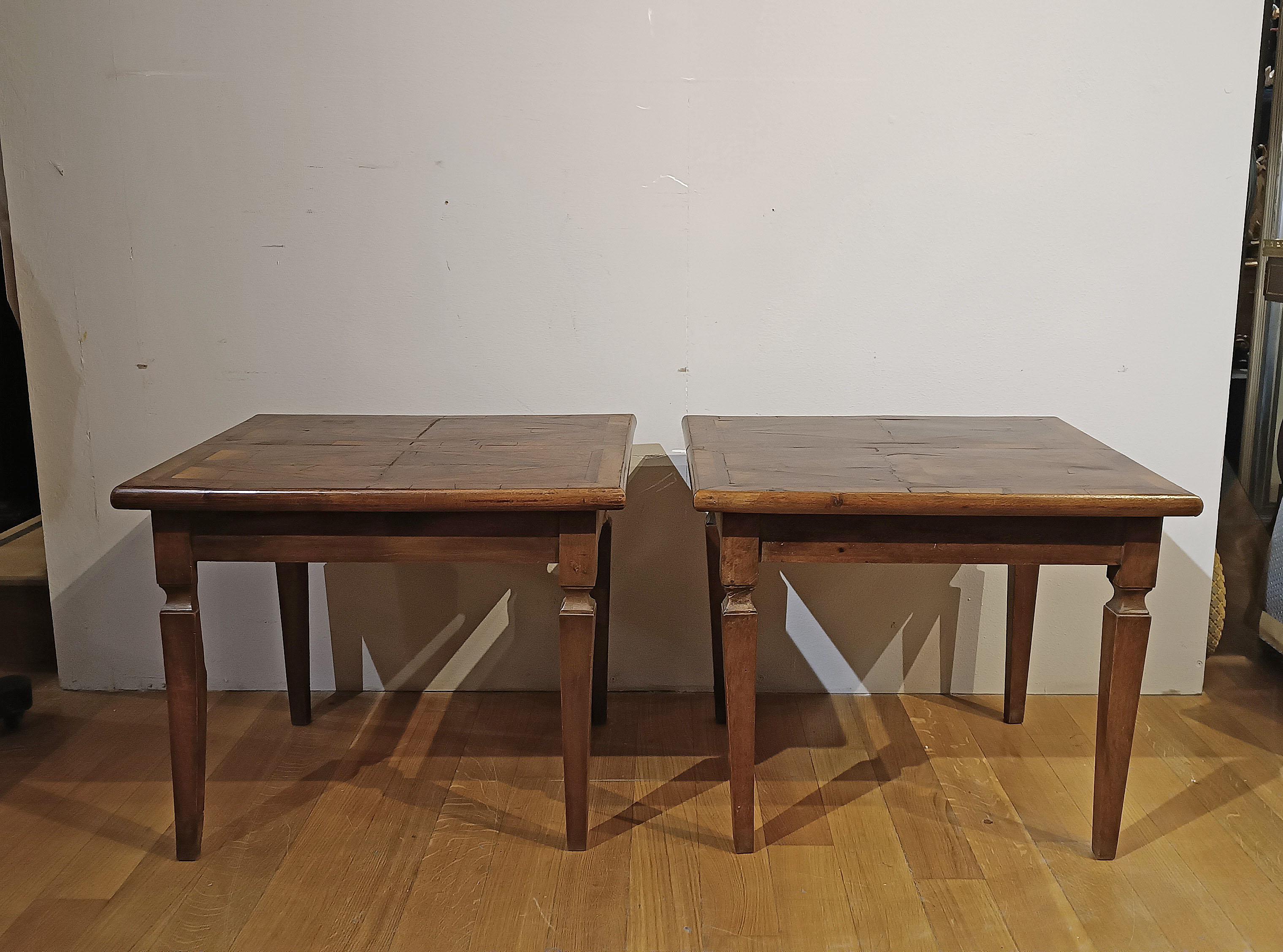Elegante paire de tables basses, plaquées et incrustées de noyer, d'olivier et d'autres bois. Les tables présentent des pieds en pyramide tronquée, typiques du style néoclassique, et des plateaux agrémentés d'incrustations géométriques qui