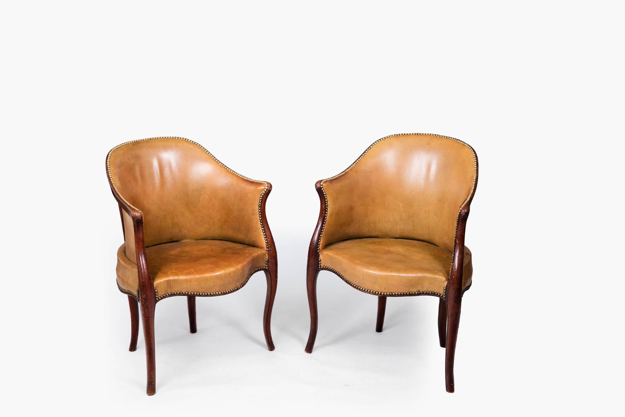 Late 18th Century pair of tub library armchairs, of carved Durmast Oak, in the Hepplewhite style. This fine pair of Georgian library chairs upholstered in a tanned leather hide are accented with brass nailhead trims. The moulded show-wood frames are