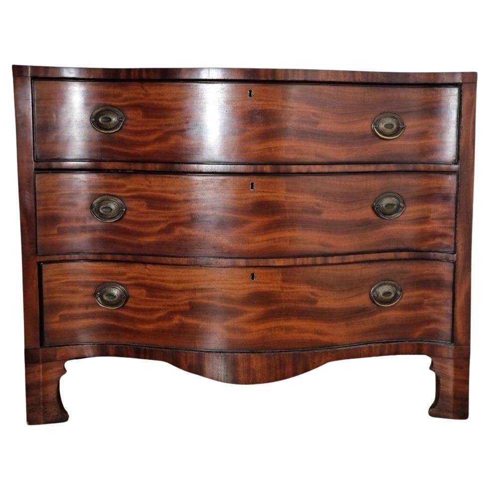 A fine George III mahogany serpentine chest of drawers with a shaped apron on bracket feet. It features three full-length drawers still retaining their original handles and smooth-running drawers. The chest is adorned with lovely figured mahogany