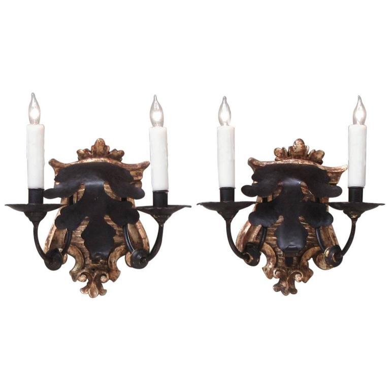 A set of four late 18th century Italian Baroque sconces, circa 1790, with silvered giltwood cartouche bases and two patinated brass and tole candle arms. The Baroque tole arms where made to left off the sconces to be carried to other rooms. The