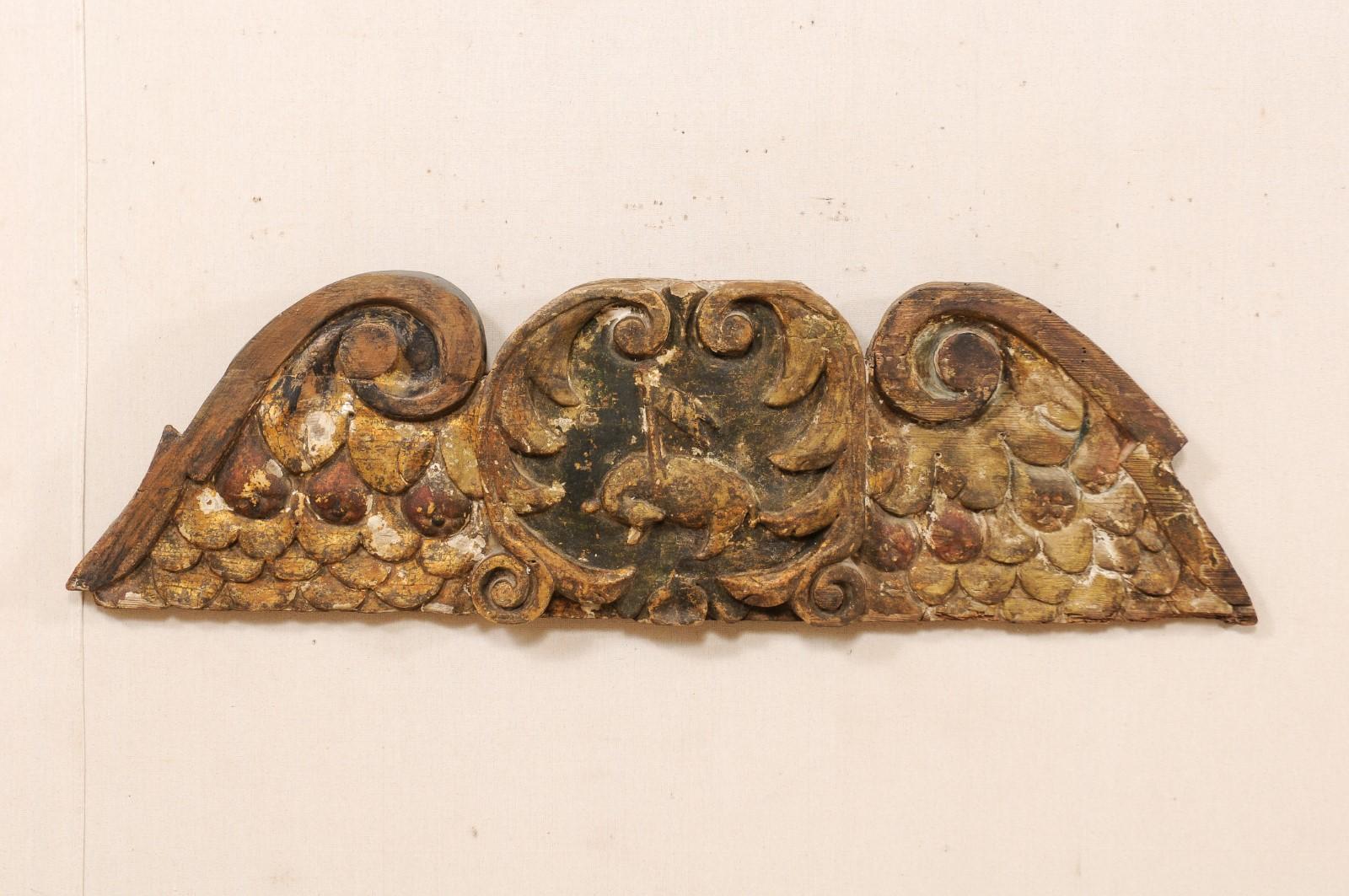 A Spanish carved wood fragment from the late 18th-early 19th century. This antique wall decoration from Spain has been hand-carved to resemble an outwardly displayed wing span, framed with volutes and feather details. There is an animal carved at