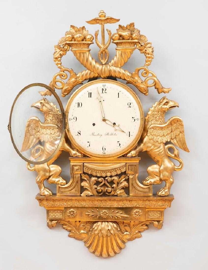 Pendule cartel néoclassique suédoise en bois doré avec des griffons gustaviens. Une taille impressionnante. Dorure originale.
Le cadran peint est signé Beurling, Stockholm pour Henrik Beurling 1758-1806.

 