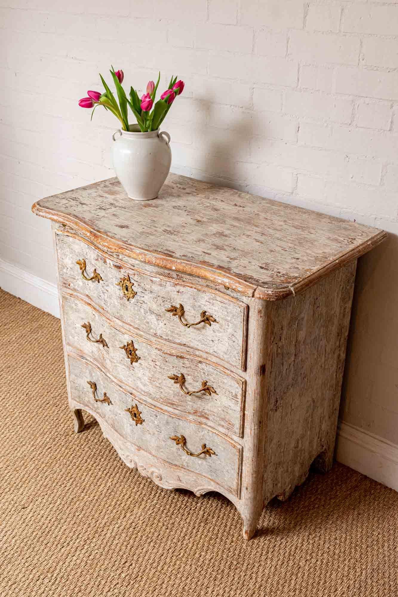 Late 18th century hand painted commode or chest of drawers. This is a substantially sturdy and well-made piece for such a small commode. It features a sliding shelf underneath the top, three curved-drawers with spring-locks and brass ornate