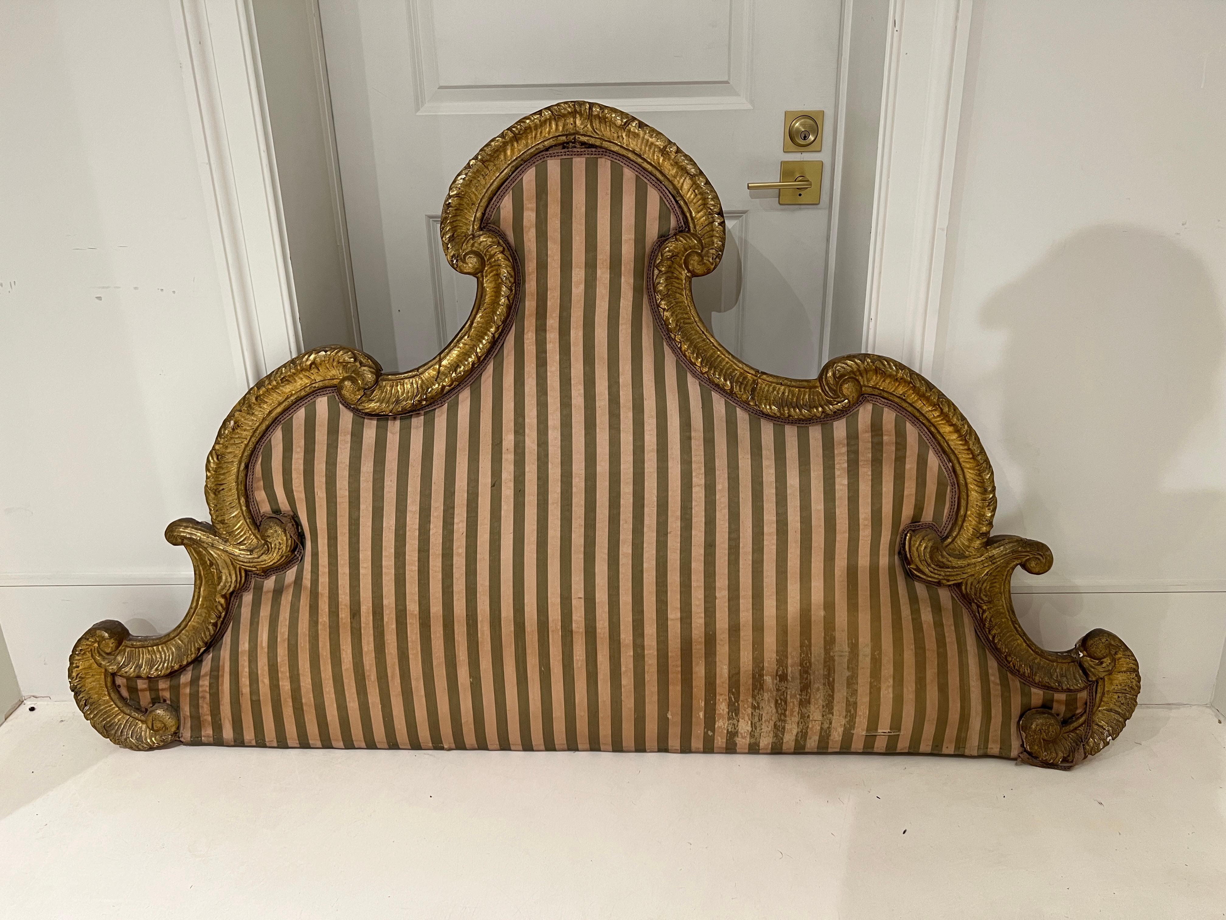 This Tuscan headboard features intricate carvings in addition to fine gold gilding. The wooden frame of the headboard remains in excellent condition. The current fabric has minor signs of aging. Reupholster to make it custom to your space.  