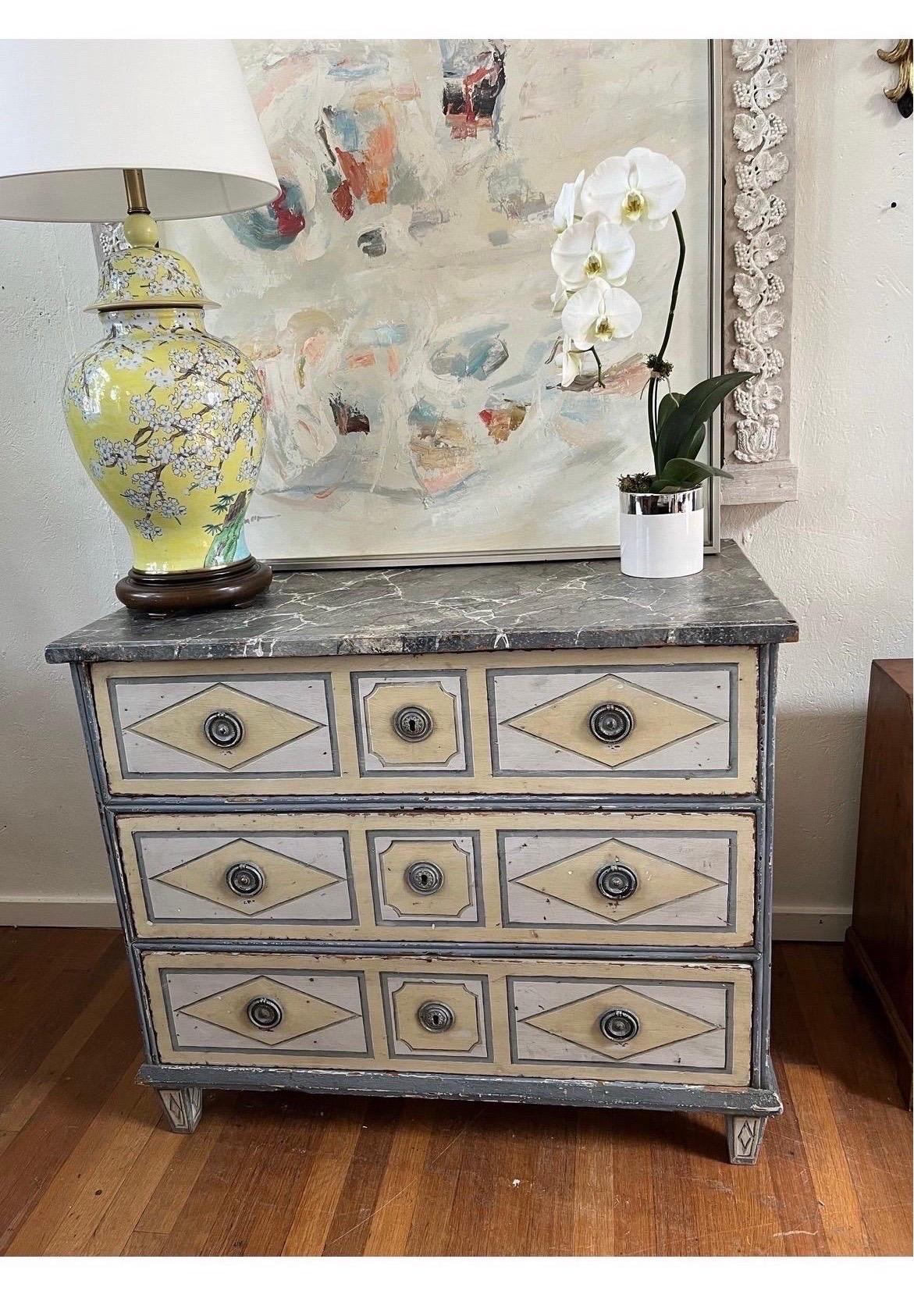 A french late 18th century three drawer commode having geometric painted panel drawers, two ring pulls on each drawer, matching painted sides and feet. Faux marble top. Distressed finish.