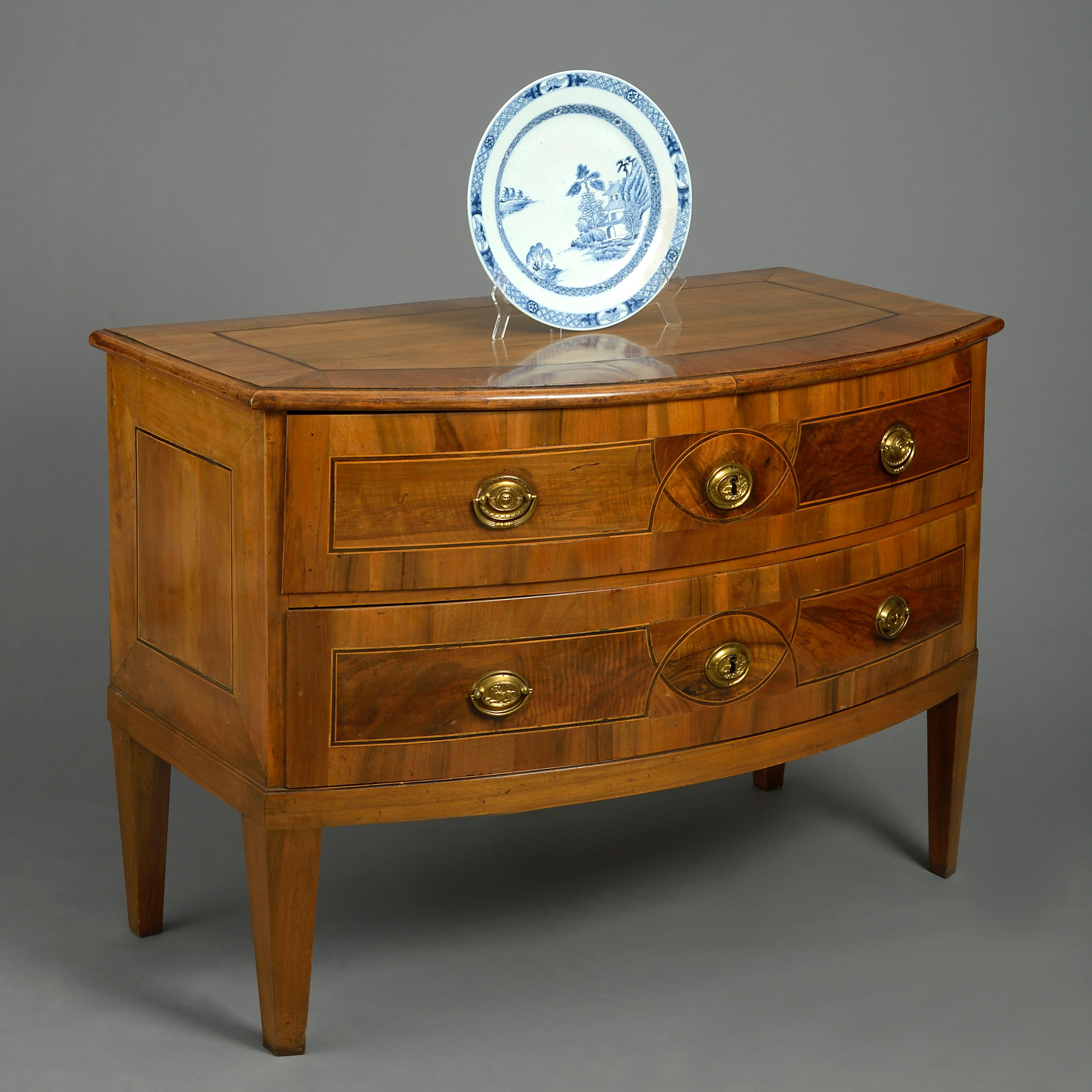 A fine late 18th century bow front commode in the neoclassical taste, the overhanging cross-banded top with ebony and boxwood stringing above two long drawers of the same, with oval brass handles and lock escutcheons, all raised on square tapering
