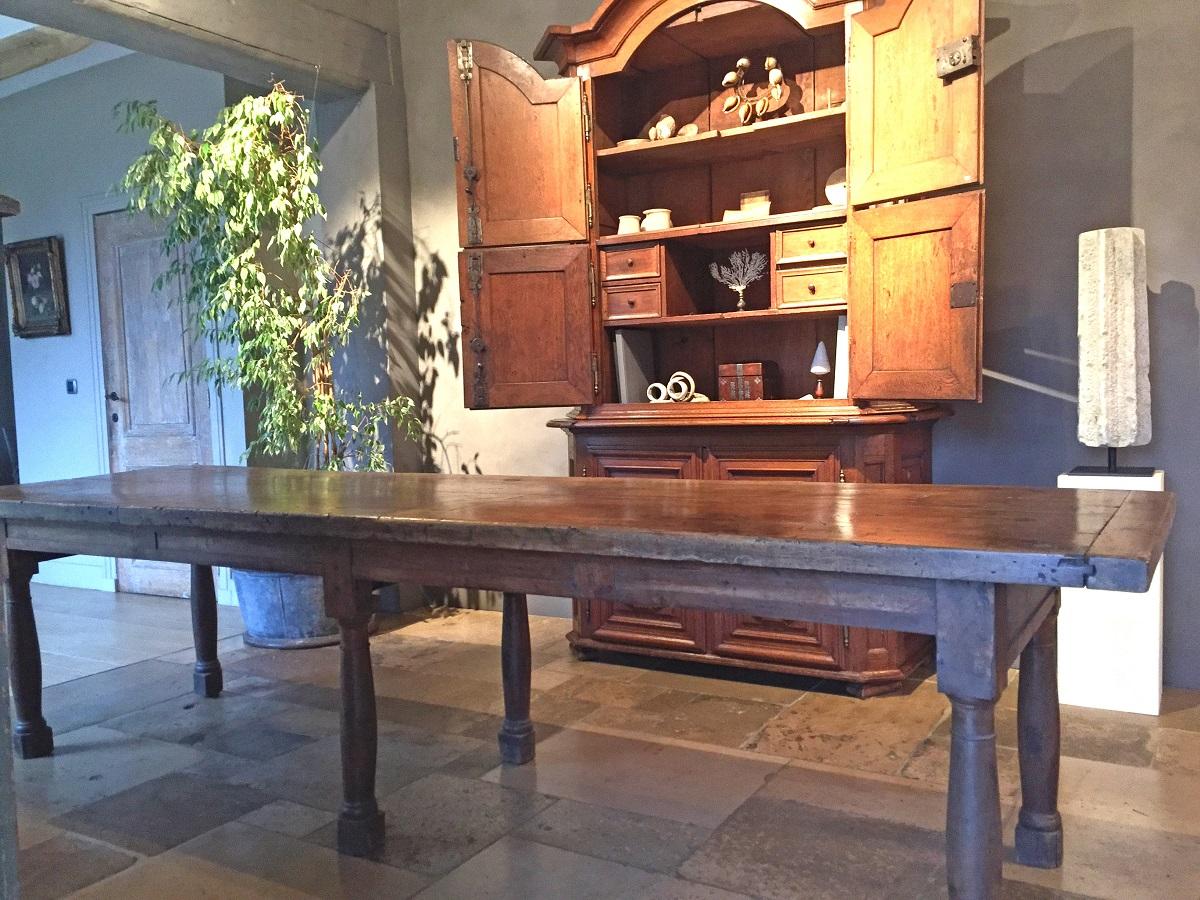 A French walnut dining table in the Directoire style. The beautifully grained and thick two plank top rests on elegant and simple turned baluster feet connected by subtle geometrically decorated planks. The top is fixed to the supports by small hand